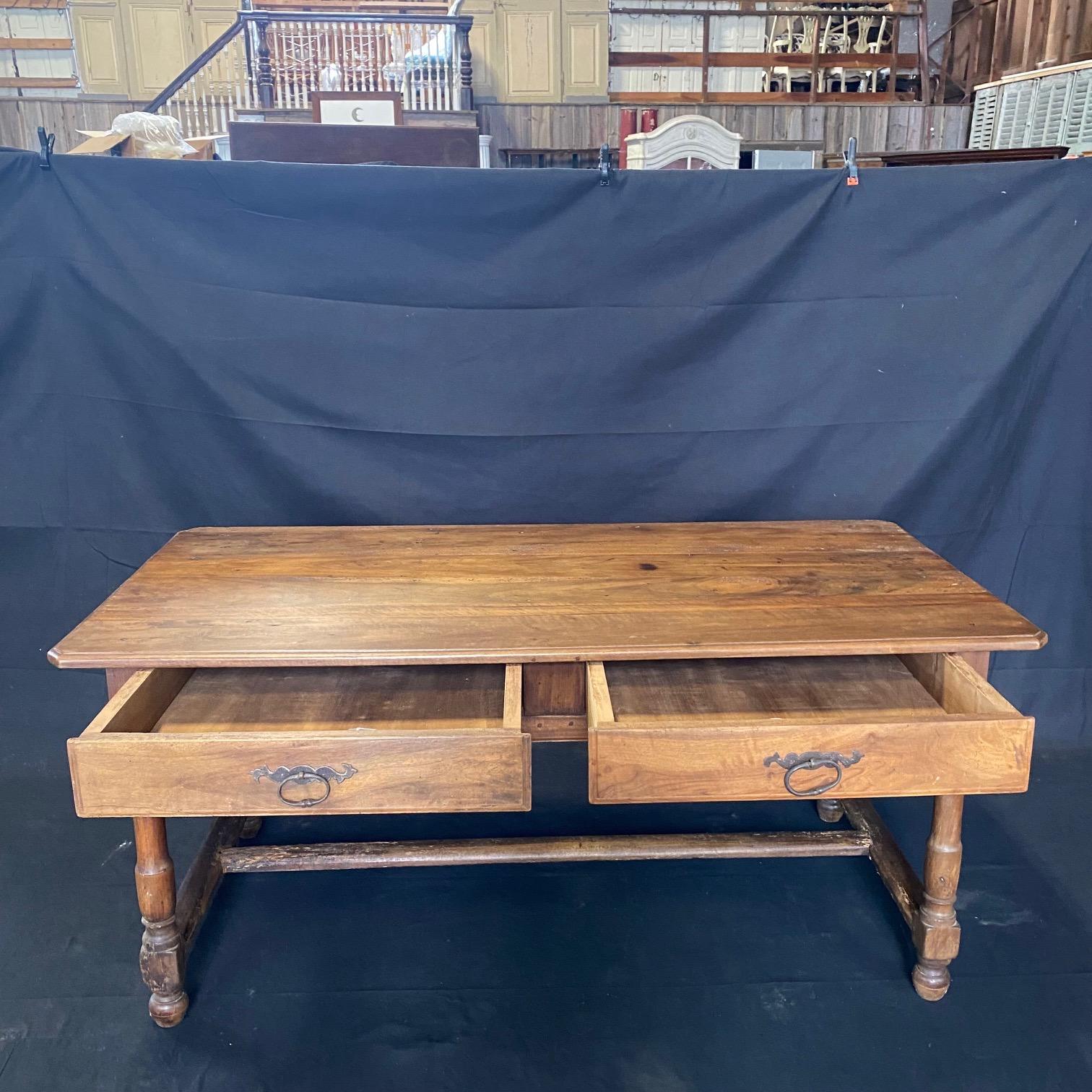This lovely walnut late 18th century French Provincial country farmhouse dining table has two generous drawers with original pulls on the front. Stretchers are sturdy on either side of classically turned legs, and used for centuries of use in a