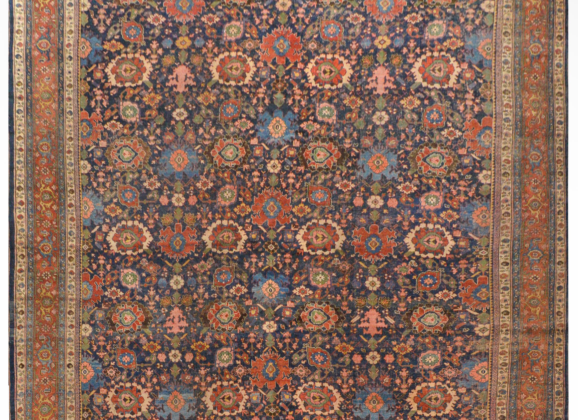 An incredible late 19th century Persian palatial-scale Bidjar rug with a fantastic large-scale floral pattern woven in crimson, indigo, gold, green, brown, and pink, all on a dark indigo background. The border is complex with a wide floral patterned