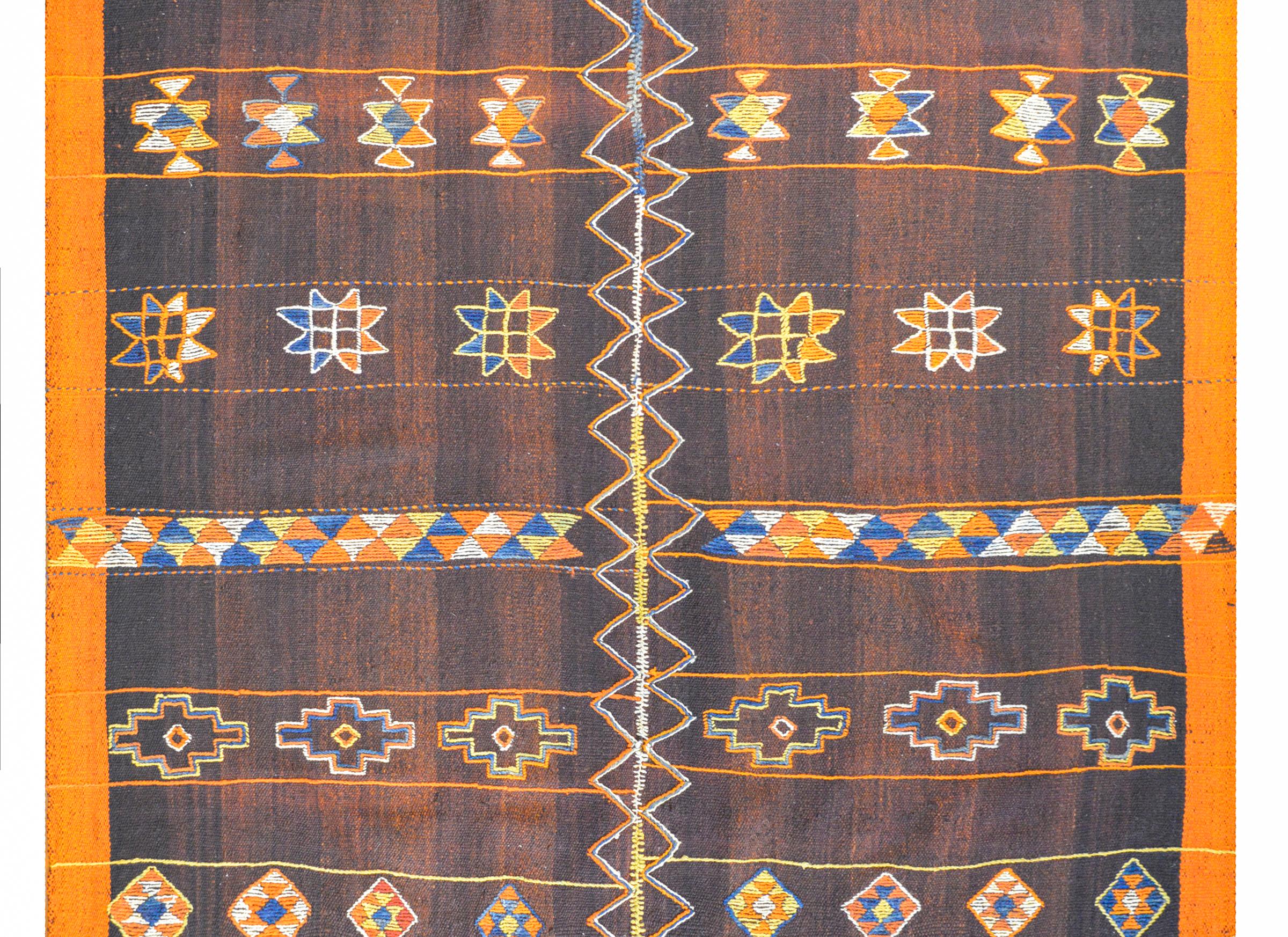 Un incredibile tappeto kilim turco della metà del XX secolo con un meraviglioso motivo a strisce che alterna fiori stilizzati e motivi geometrici tessuti in lana tinta al vegetale color indaco, oro, arancio e bianco.