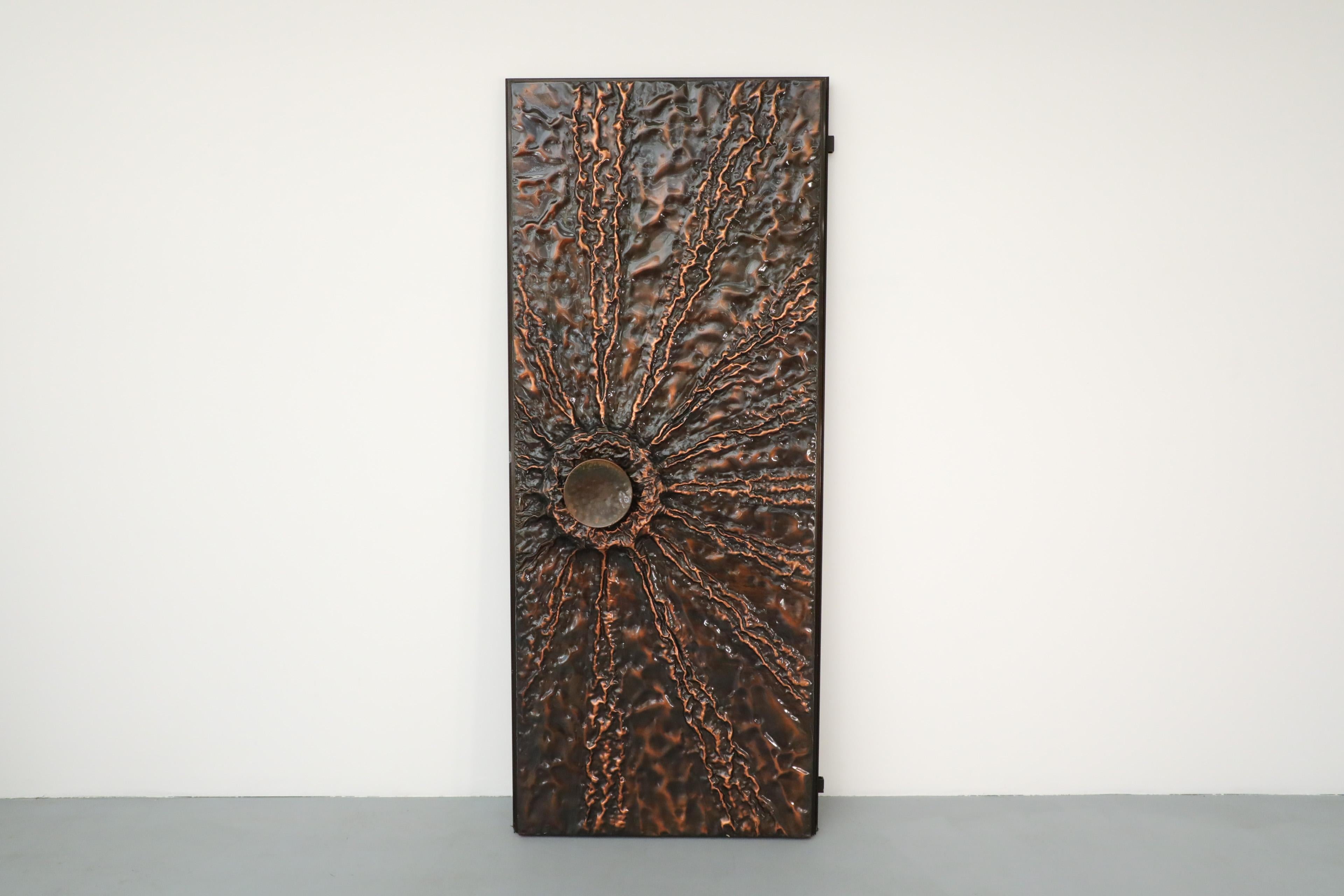 Incredible Brutalist copper entrance door with beautifully textured sunburst design and oversized door handle. This large and heavy door is embossed on the outside only with the reverse side consisting of a framed white stained wood panel a handle