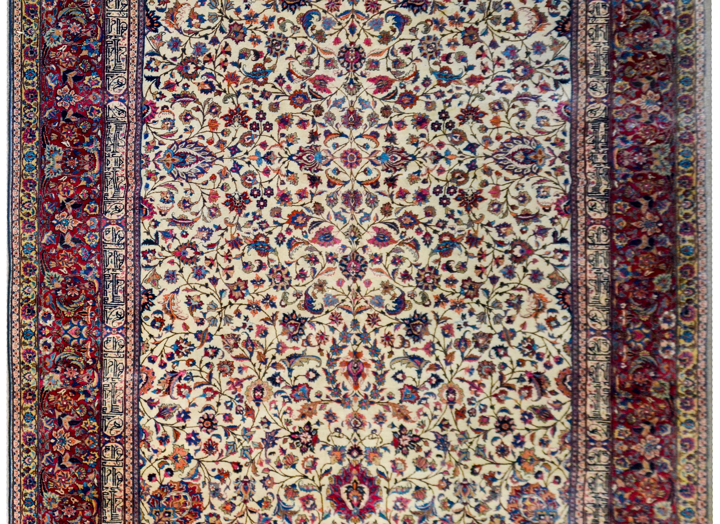 An incredible monumental early 20th century Meshed rug with a densely woven mirrored pattern of multicolored flowering scrolling vines woven in light and dark indigo, pink, orange, crimson, brown, and black wool on a natural cream colored wool
