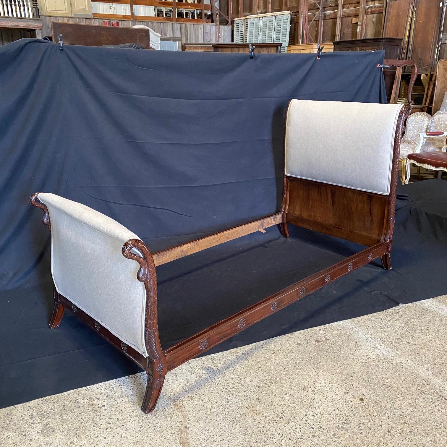 Early 20th century French Empire daybed featuring carved swan neck ends. Crafted from rich walnut having gorgeous neoclassical motifs of rosettes and acanthus leaves. Supported by carved sloping tapered legs and new high quality upholstery. Will