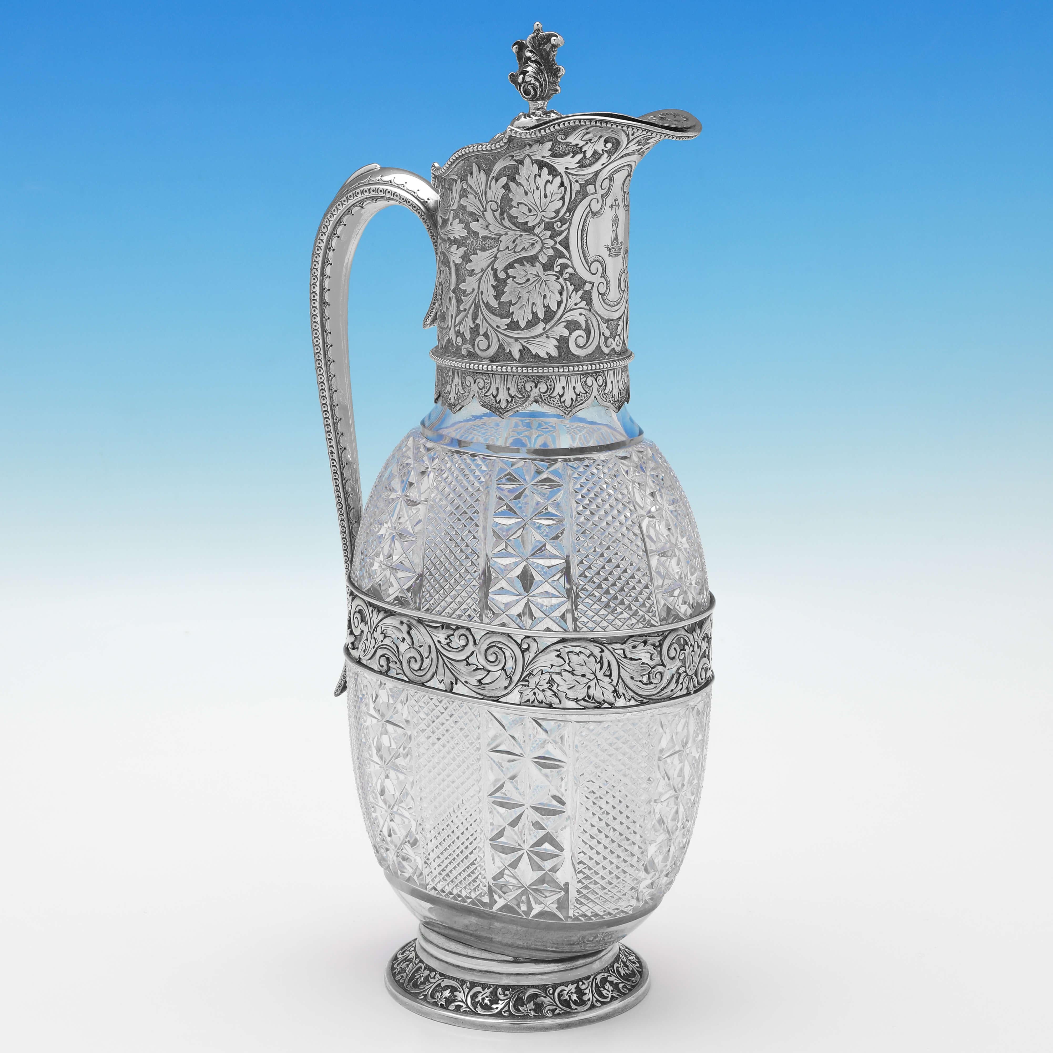 Hallmarked in London in 1889 by Edgar Finley & Hugh Taylor, this stunning pair of Antique Sterling Silver Claret Jugs, are ornate in design, featuring wonderful decoration to the silver mounts, heavily cut glass bodies, and engraved crests to the
