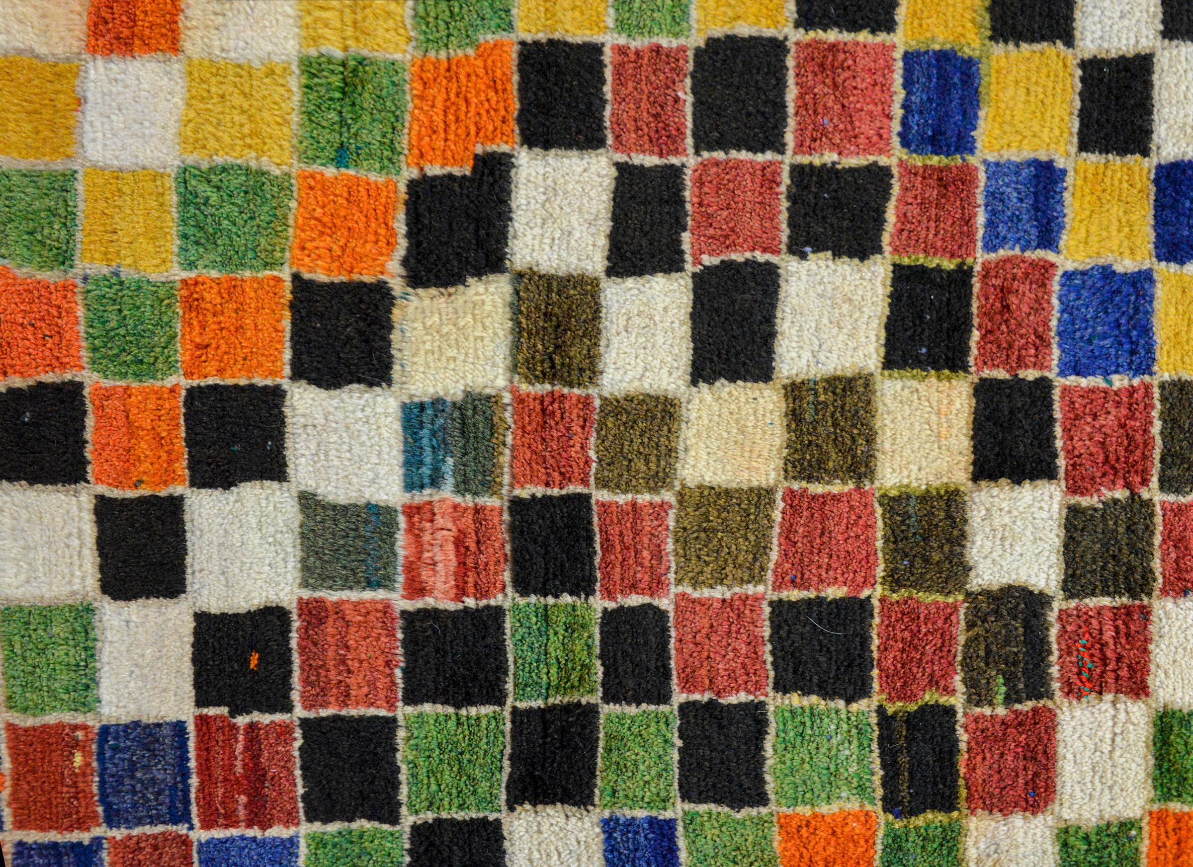 An incredible vintage Persian hand-knotted Gabbeh rug with a multi-colored checkerboard pattern woven in myriad colors including orange, gold, green, black, white, and indigo, and surrounded by a thin zigzag patterned border.