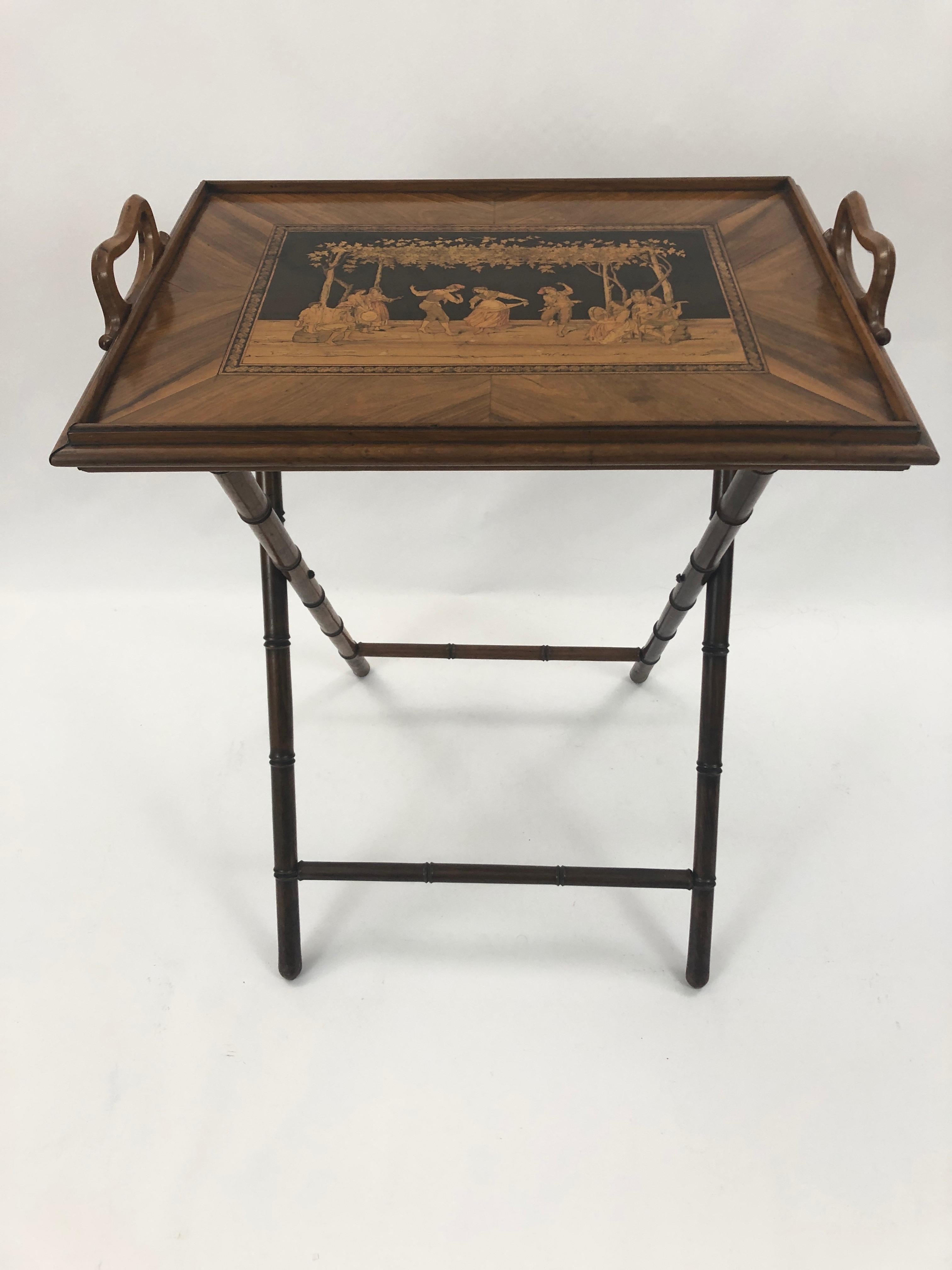 A splendid walnut inlaid tray table having a tray top on faux bamboo base with checkerboard on one side, and gorgeous intricate figural decoration on the other. The contrast of light and honey colored woods against a black background is especially