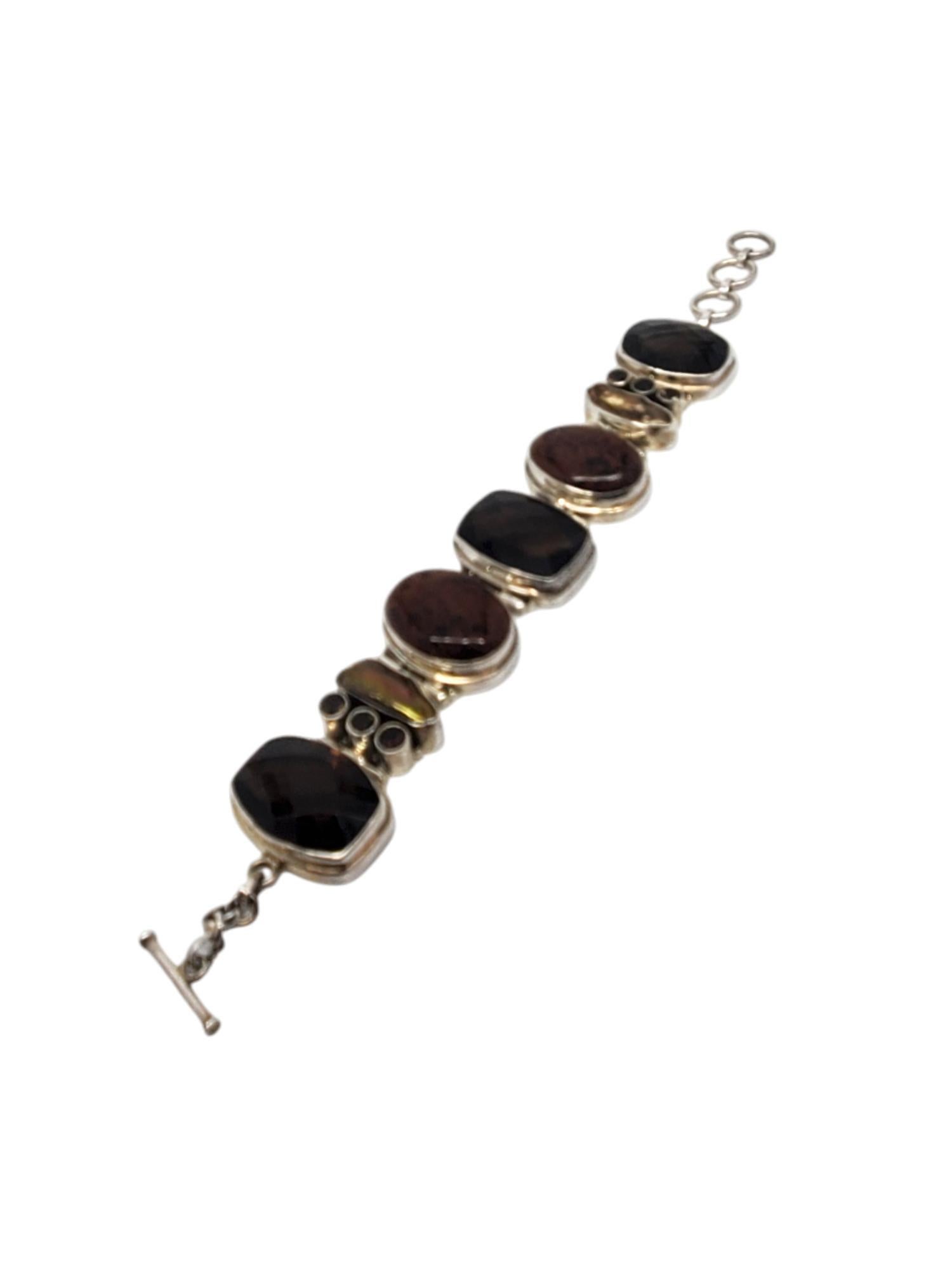 Inde 925 Large bracelet à charnière marron multi pierres -

Ce bracelet vintage à charnière est composé de multiples pierres ovales à facettes foncées et mouchetées de brun serties dans de l'argent sterling avec un fermoir à bascule de l'Inde