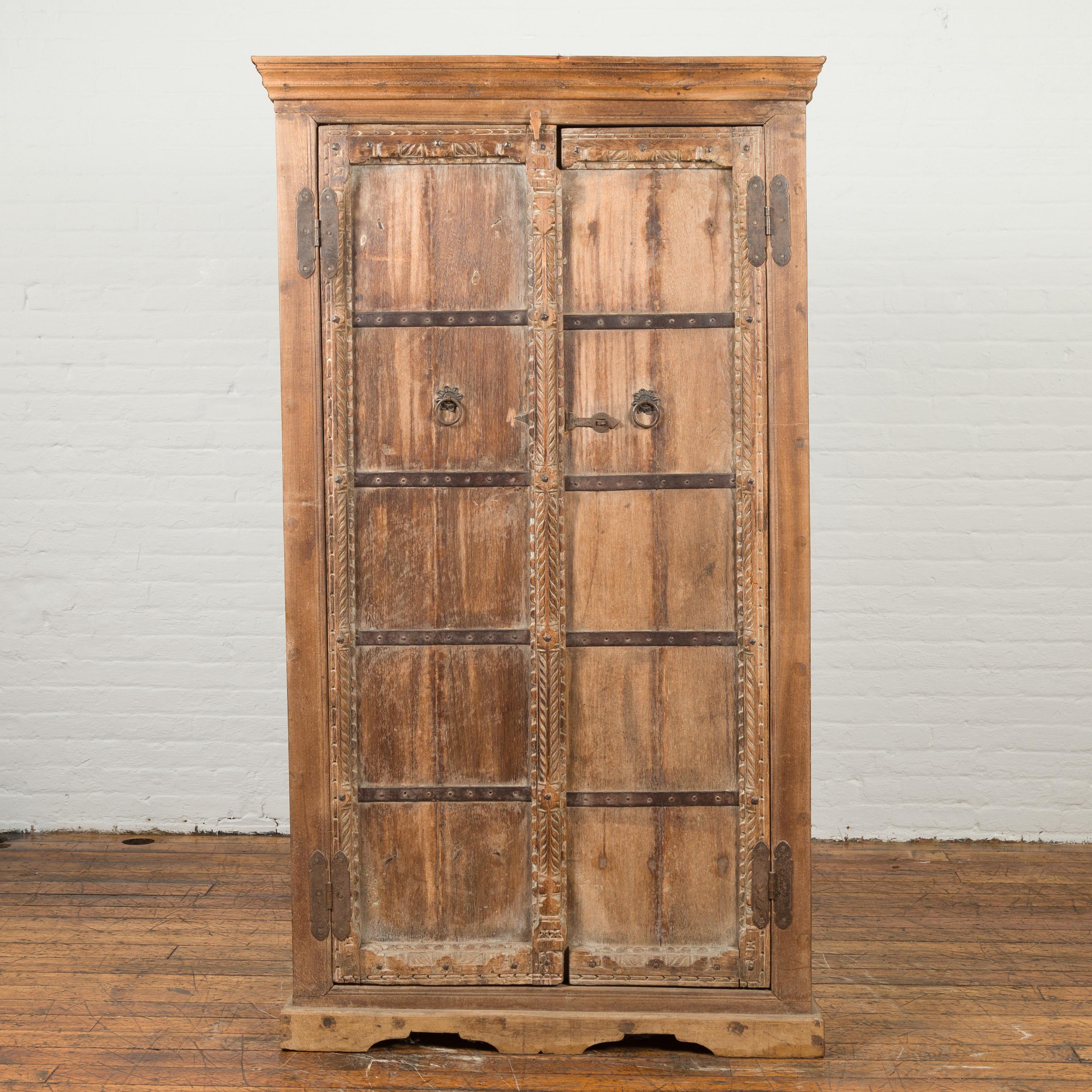 An Indian sheesham wood cabinet from the 19th century, with distressed patina, carved doors and iron accents. Created in India during the 19th century, this sheesham wood tall cabinet features a molded cornice sitting above two carved doors