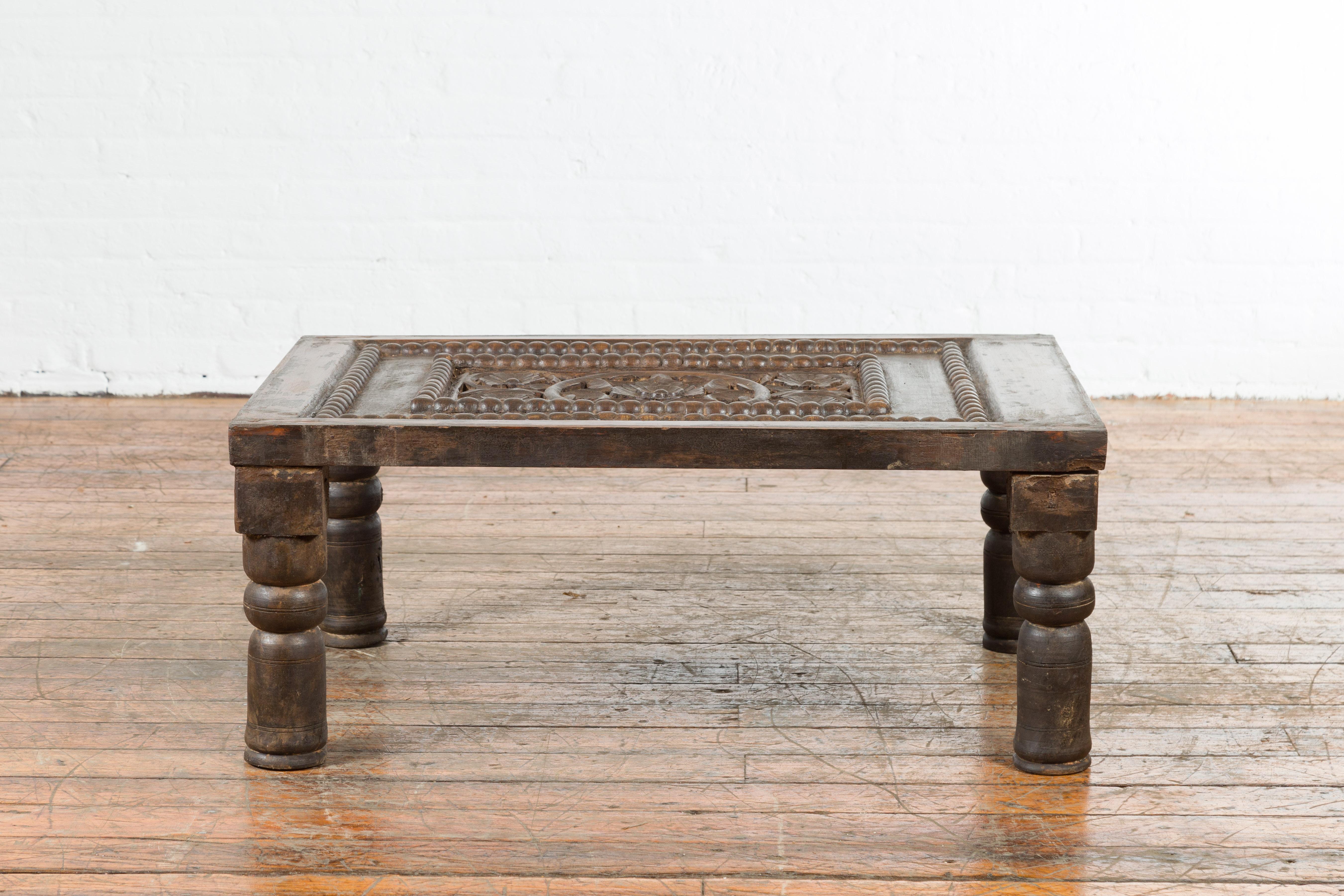 An Indian antique small coffee table from the 19th century, with carved wooden floral motifs and baluster legs. Created in India during the 19th century, this small coffee table features a rectangular top showcasing carved and pierced floral motifs