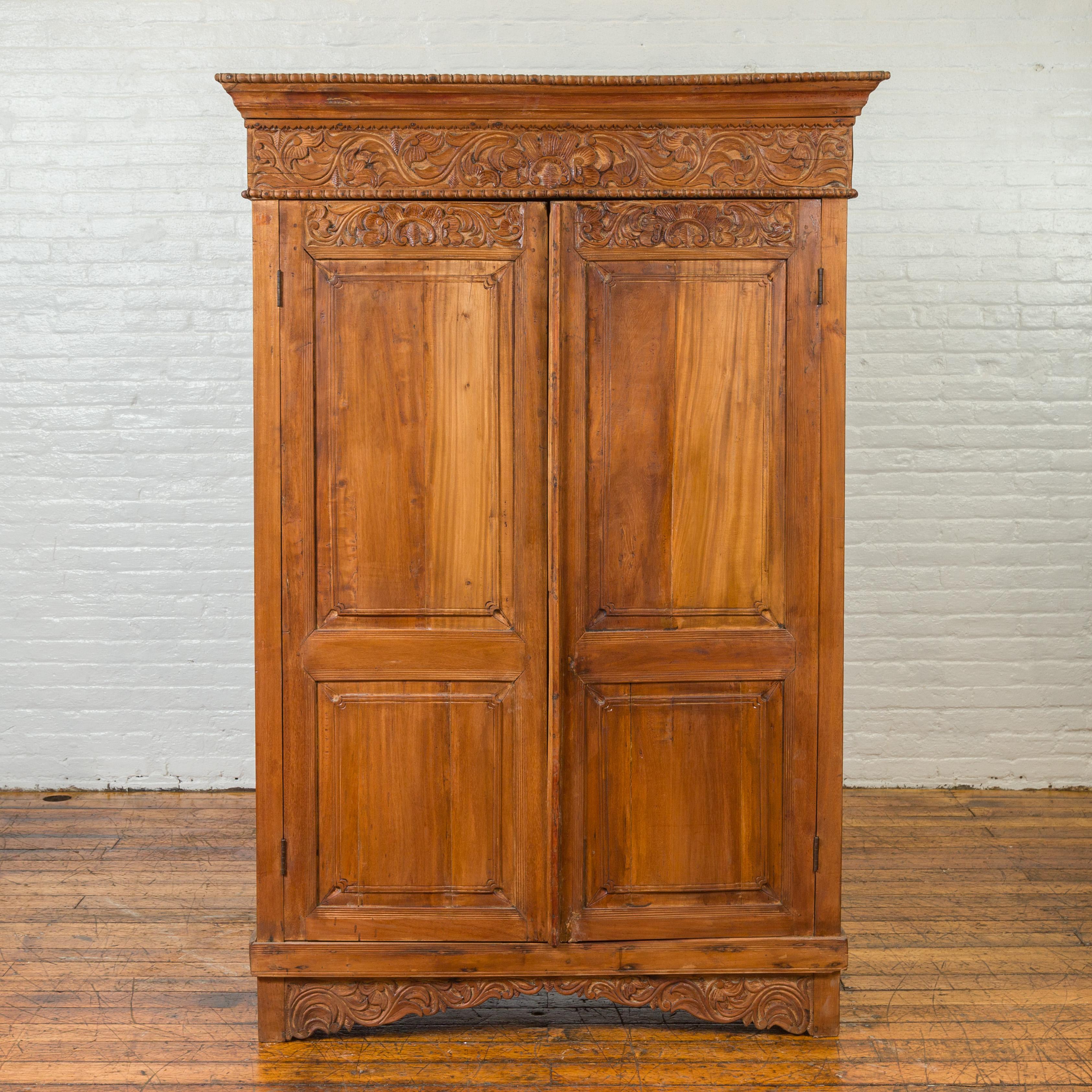 An Indian carved wooden tall cabinet from the 19th century, with scrolling foliage and beaded accents. Crafted in India during the 19th century, this tall cabinet captivates us with its warm patina and delicately carved motifs. A cornice, adorned