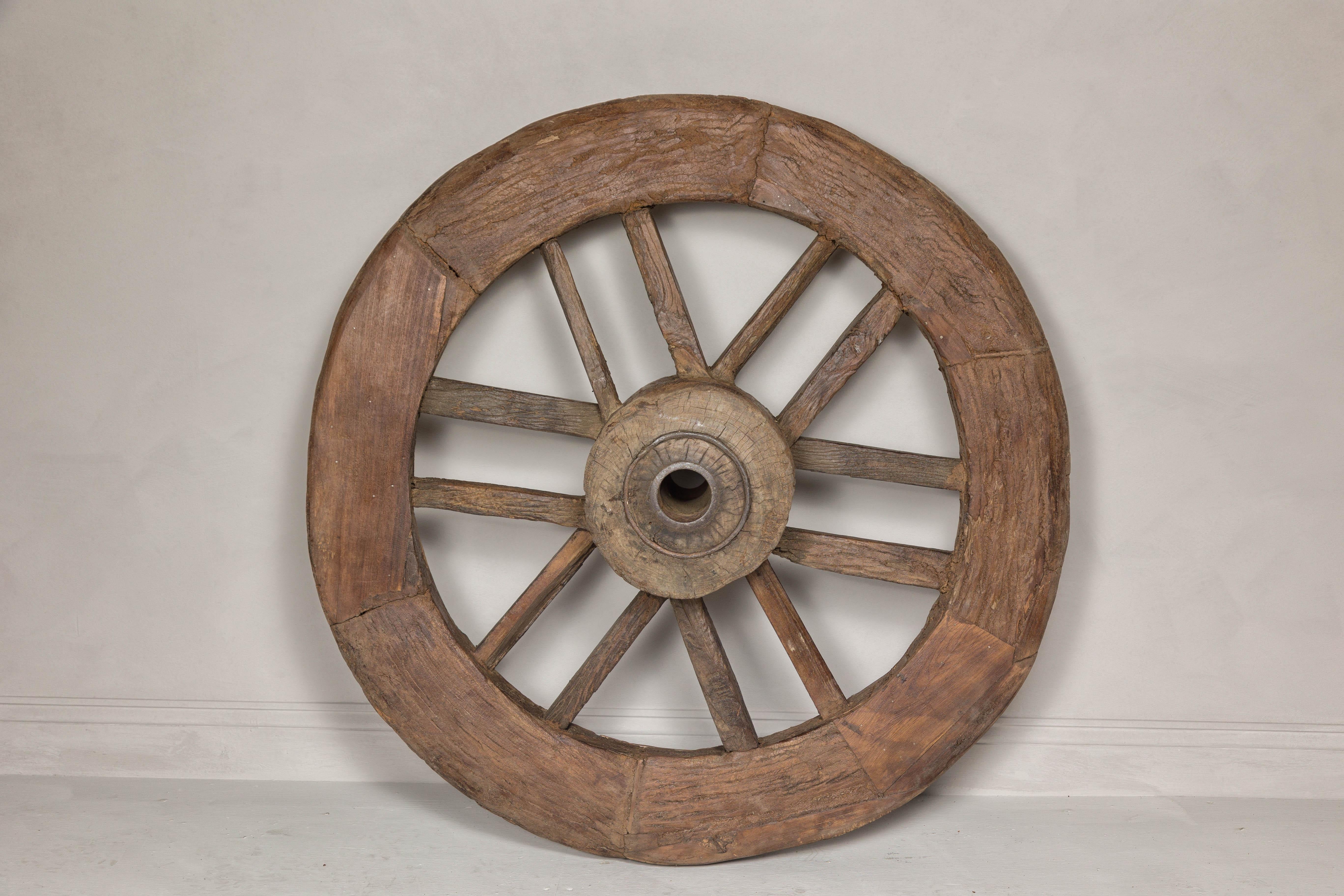 An antique Indian wood and metal cart wheel with great rustic character. This antique Indian cart wheel, crafted from wood and metal, showcases an exceptional rustic character that speaks volumes of its historical and cultural past. The wheel is