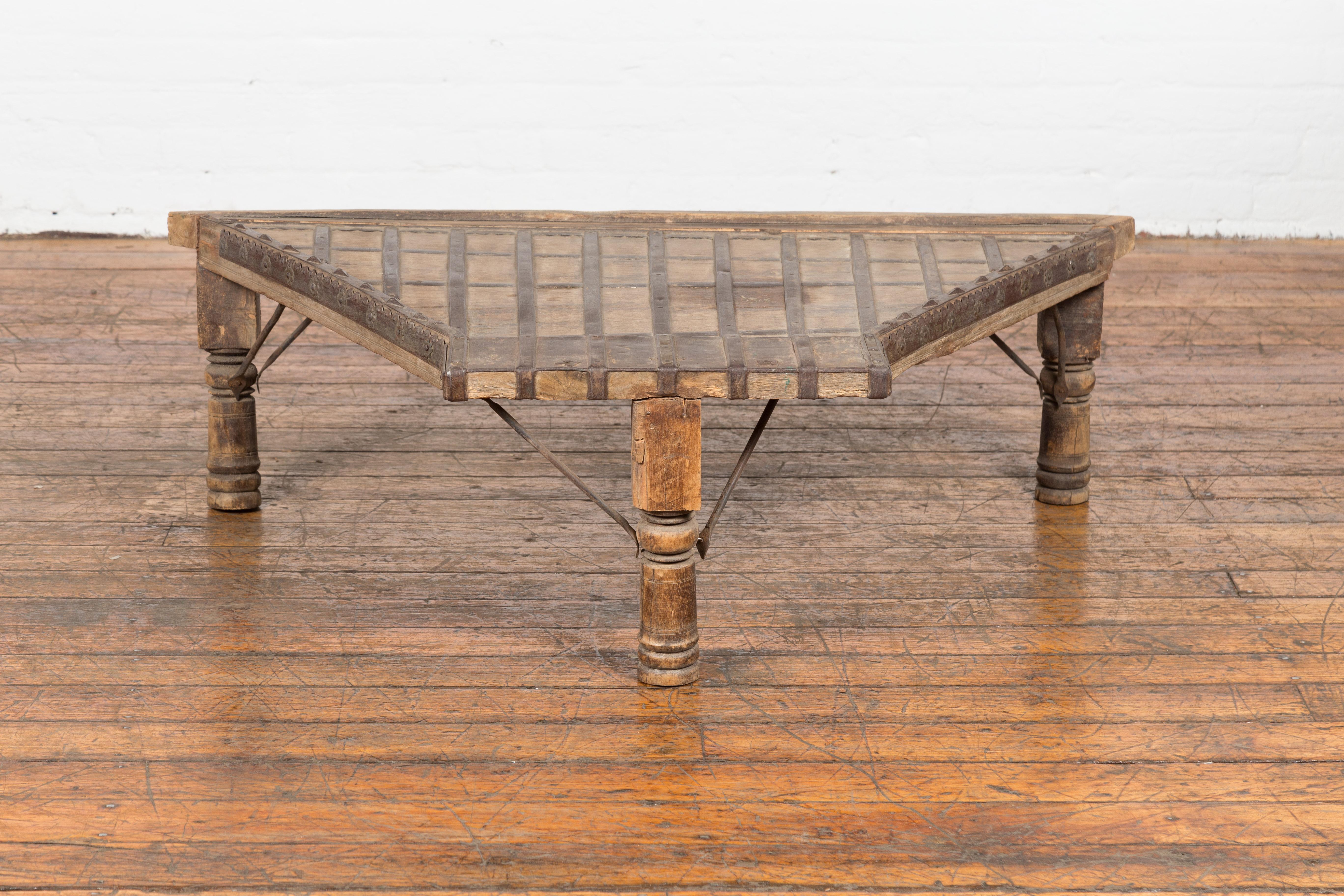 An antique rustic Indian handmade coffee table from the 19th century with trapezoidal top, protruding front, iron stretchers, petite rosettes, turned baluster legs and weathered patina. This antique rustic Indian handmade coffee table from the 19th