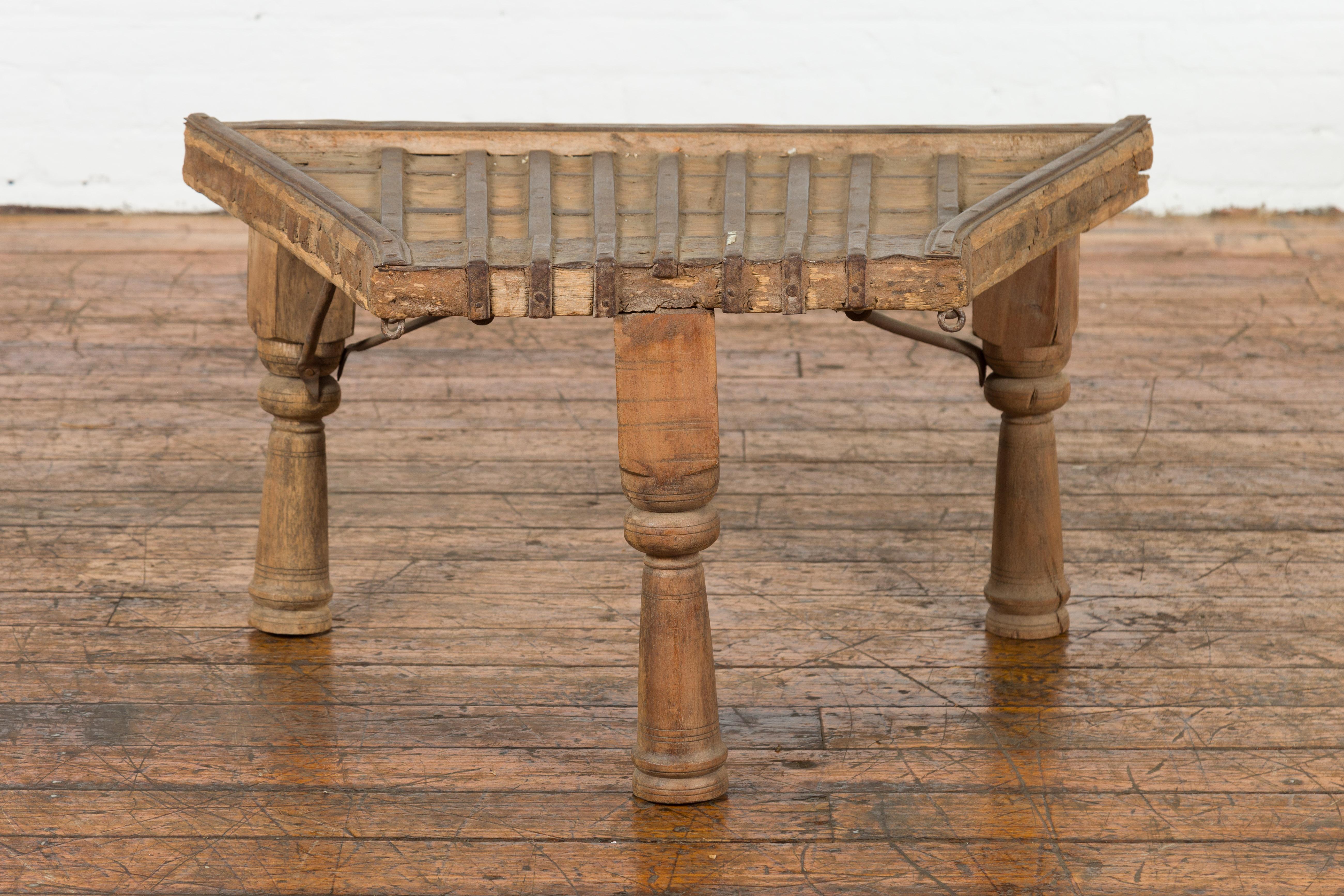 An antique rustic Indian handmade coffee table from the 19th century with trapezoidal top, protruding front, iron stretchers, turned baluster legs and weathered patina. Take a journey back in time with this 19th-century rustic Indian handmade coffee