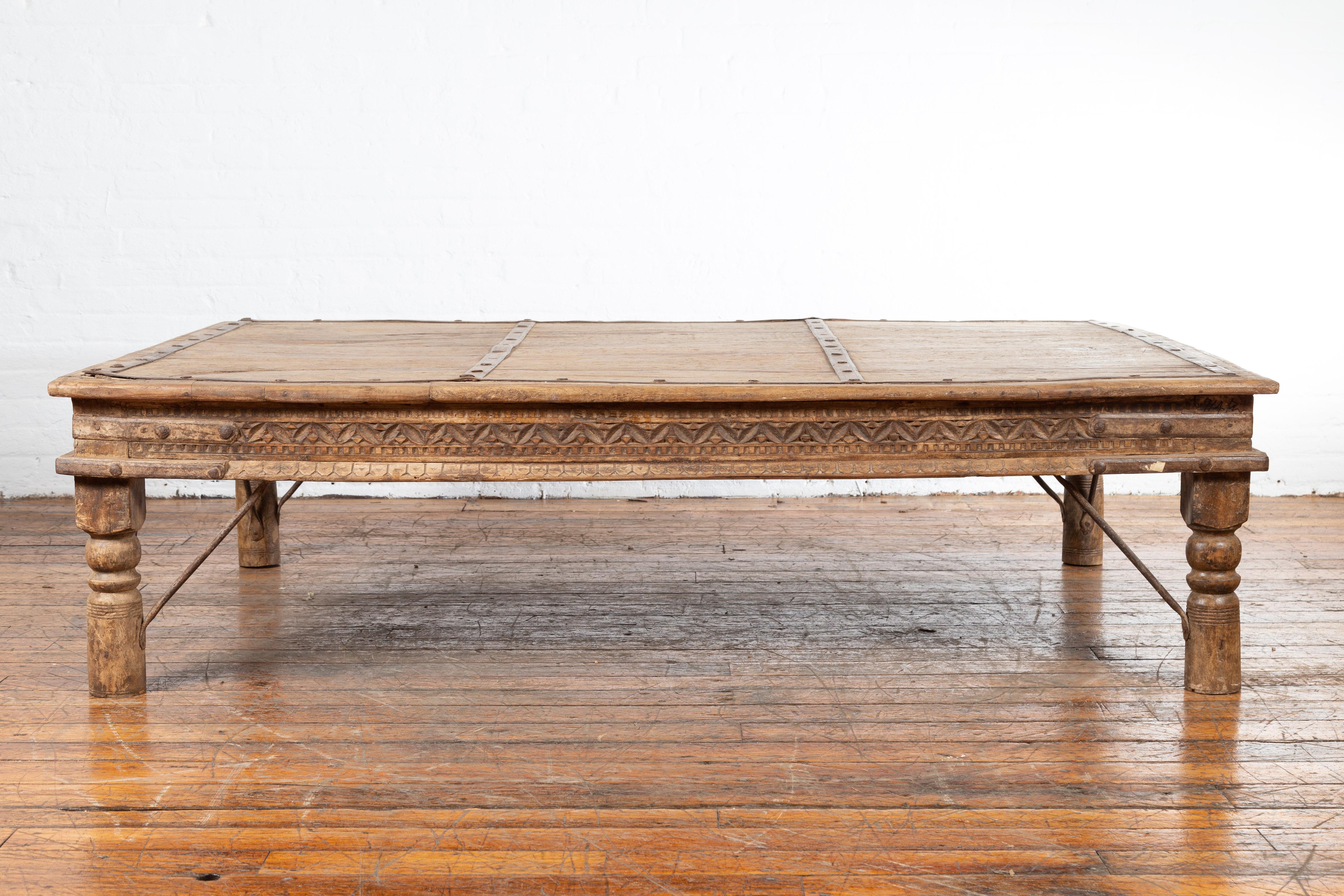 An Indian antique courtyard door from the 19th century, made into a coffee table with carved geometric motifs, baluster legs, iron accents and natural patina. Created in India during the 19th century, this courtyard door has been transformed into a