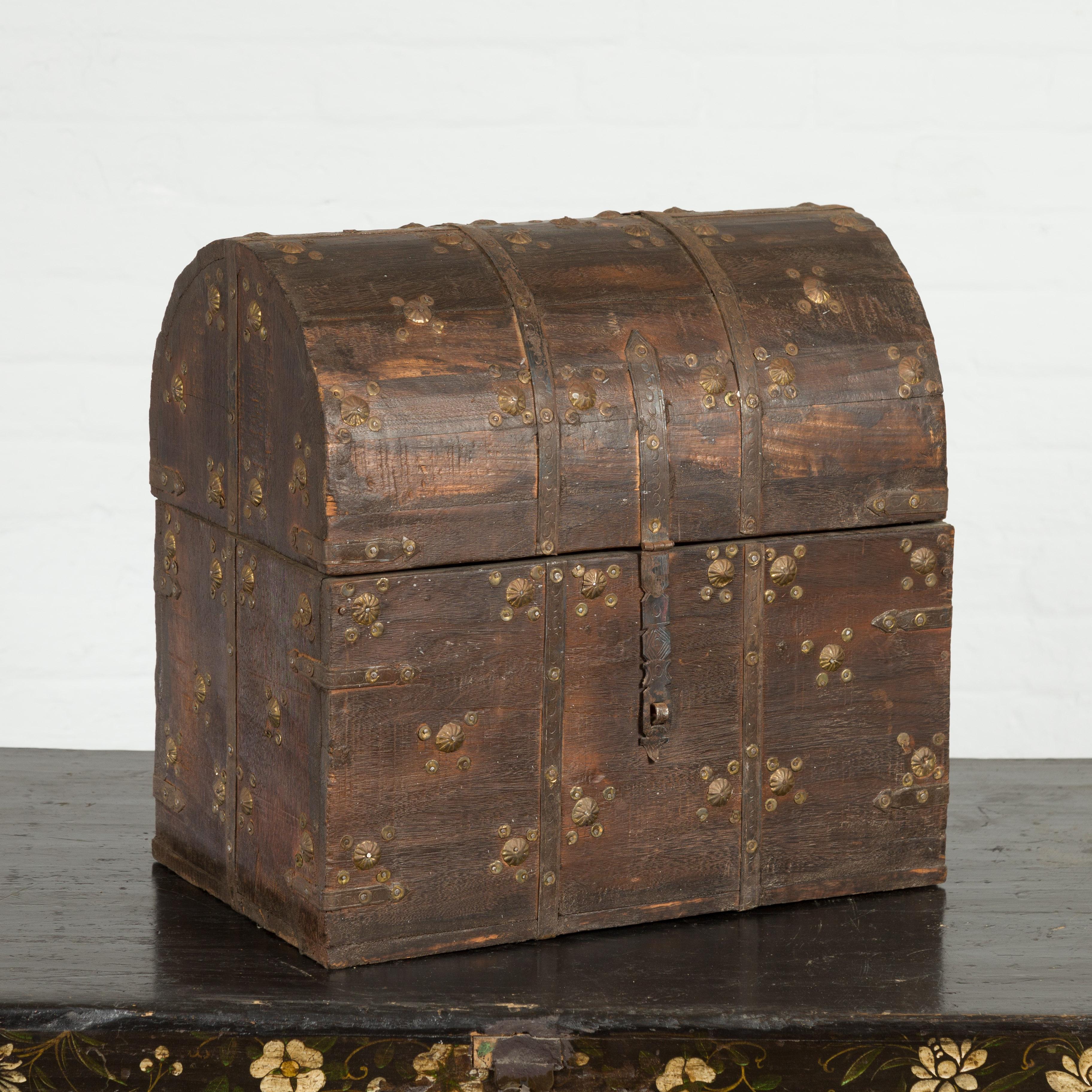 An Indian antique wooden treasure chest from the 19th century, with dome top and metal accents. Created in India during the 19th century, this treasure chest captures our attention with its distressed wooden structure accented with petite gilt metal