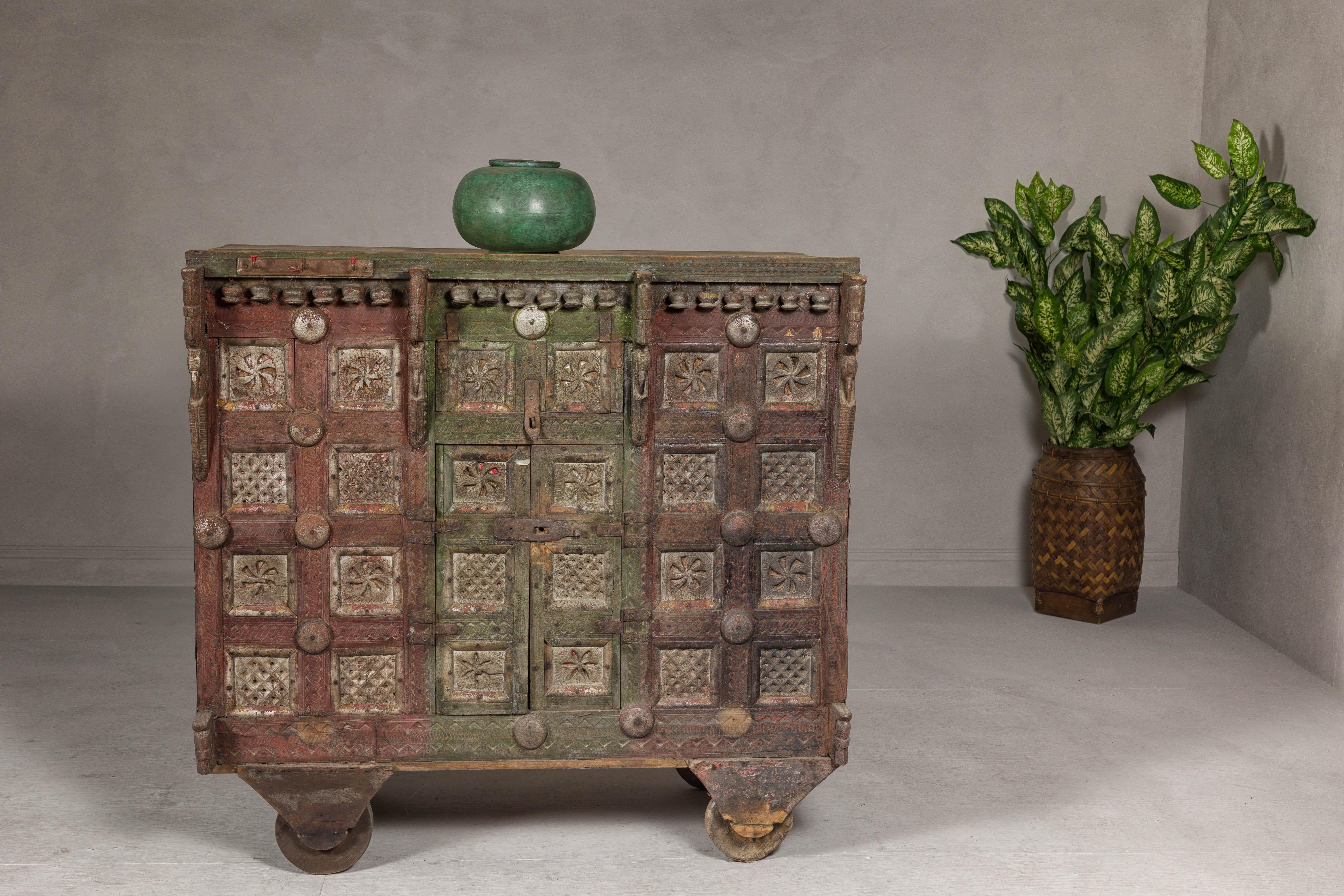 An antique Indian carved wooden Damachiya dowry cabinet mounted on wheels from the 19th century with polychrome décor and rustic character. This exquisite antique Indian Damachiya dowry cabinet from the 19th century captivates with its intricate