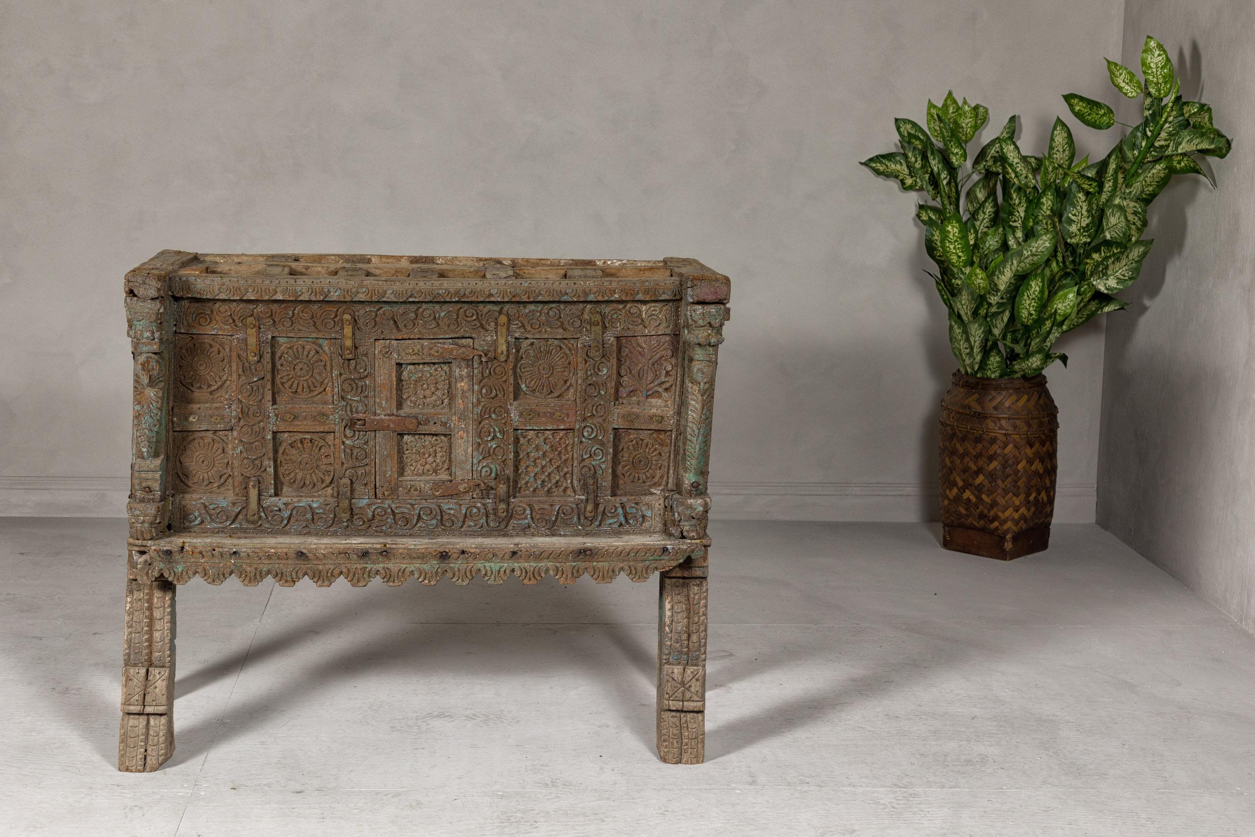 An antique rustic Indian Damachiya wedding cabinet on legs from the 19th century with abundantly carved décor and traces of paint. This 19th-century rustic Indian Damachiya wedding cabinet is a magnificent example of traditional craftsmanship,