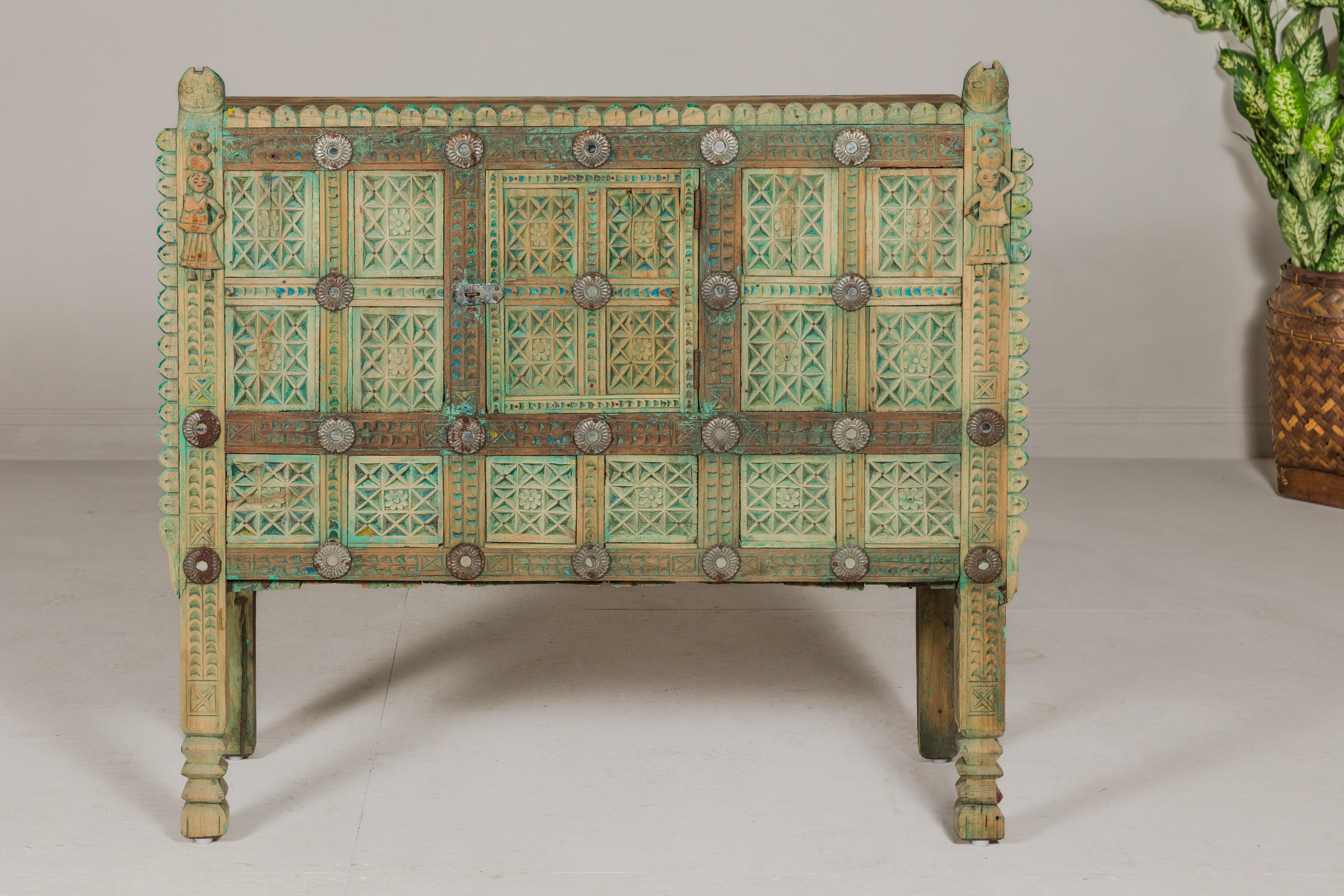 An Indian green painted Damachiya wedding cabinet on legs from the 19th century, with abundant carved décor. This 19th-century Indian Damachiya wedding cabinet, resplendent in a soft green paint, is a captivating piece of cultural heritage and