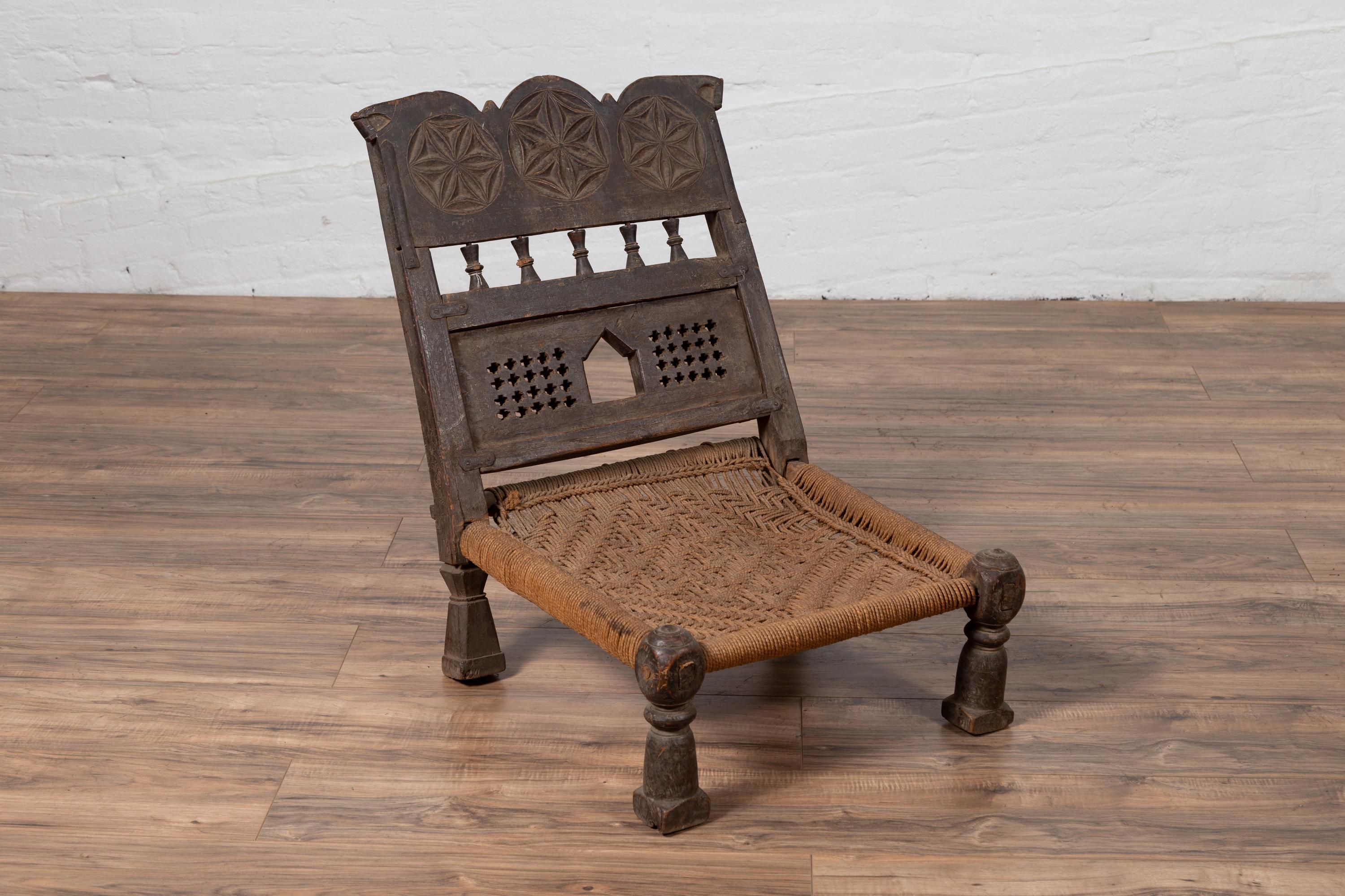 20th Century Indian Antique Rustic Low Seat Wooden Chair with Carved Rosettes and Rope Seat For Sale