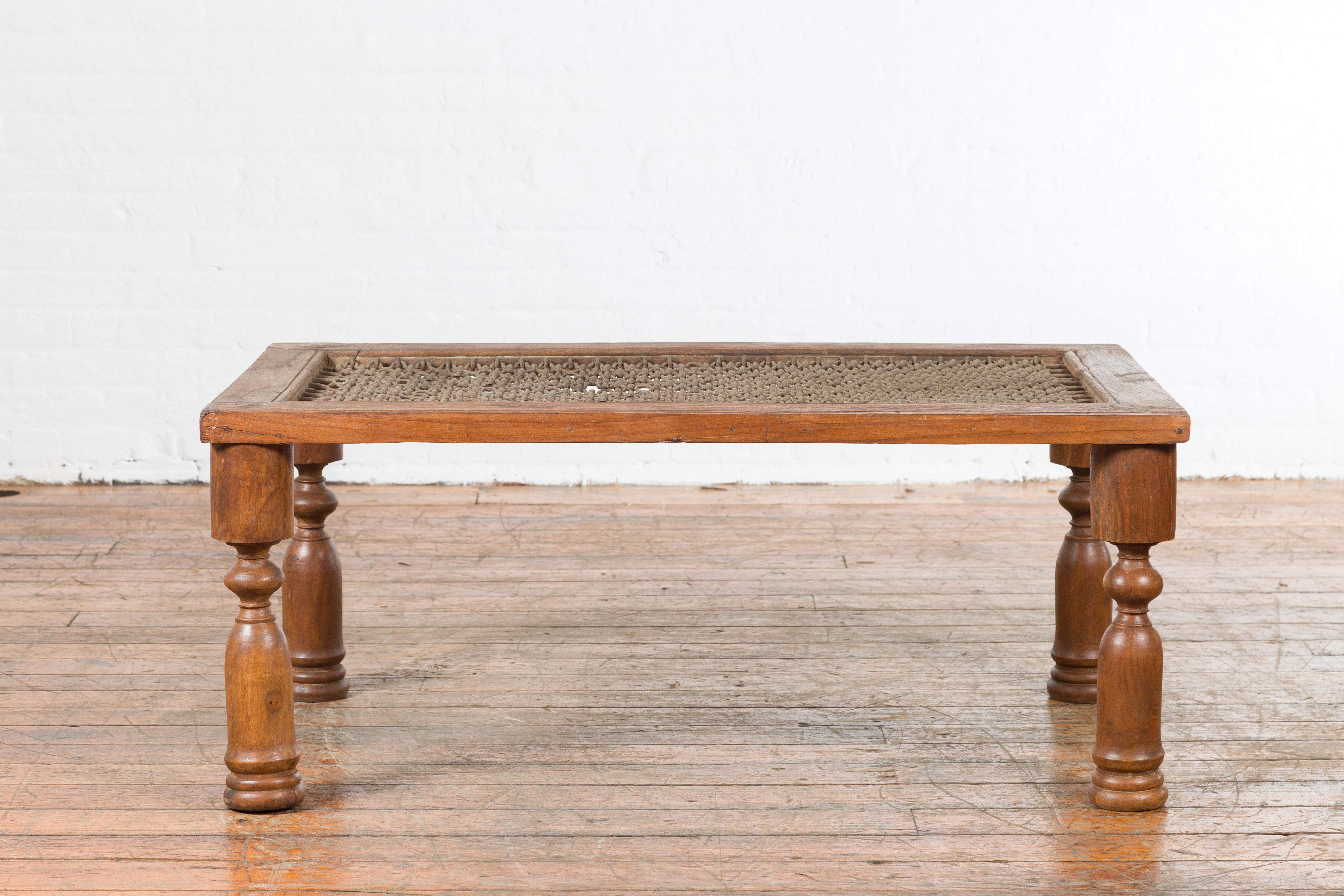 An antique Indian window grate from the 19th century, made into a coffee table with baluster legs. Created in India during the 19th century, this coffee table features an iron grate top with geometric patterns, resting on four turned baluster legs.