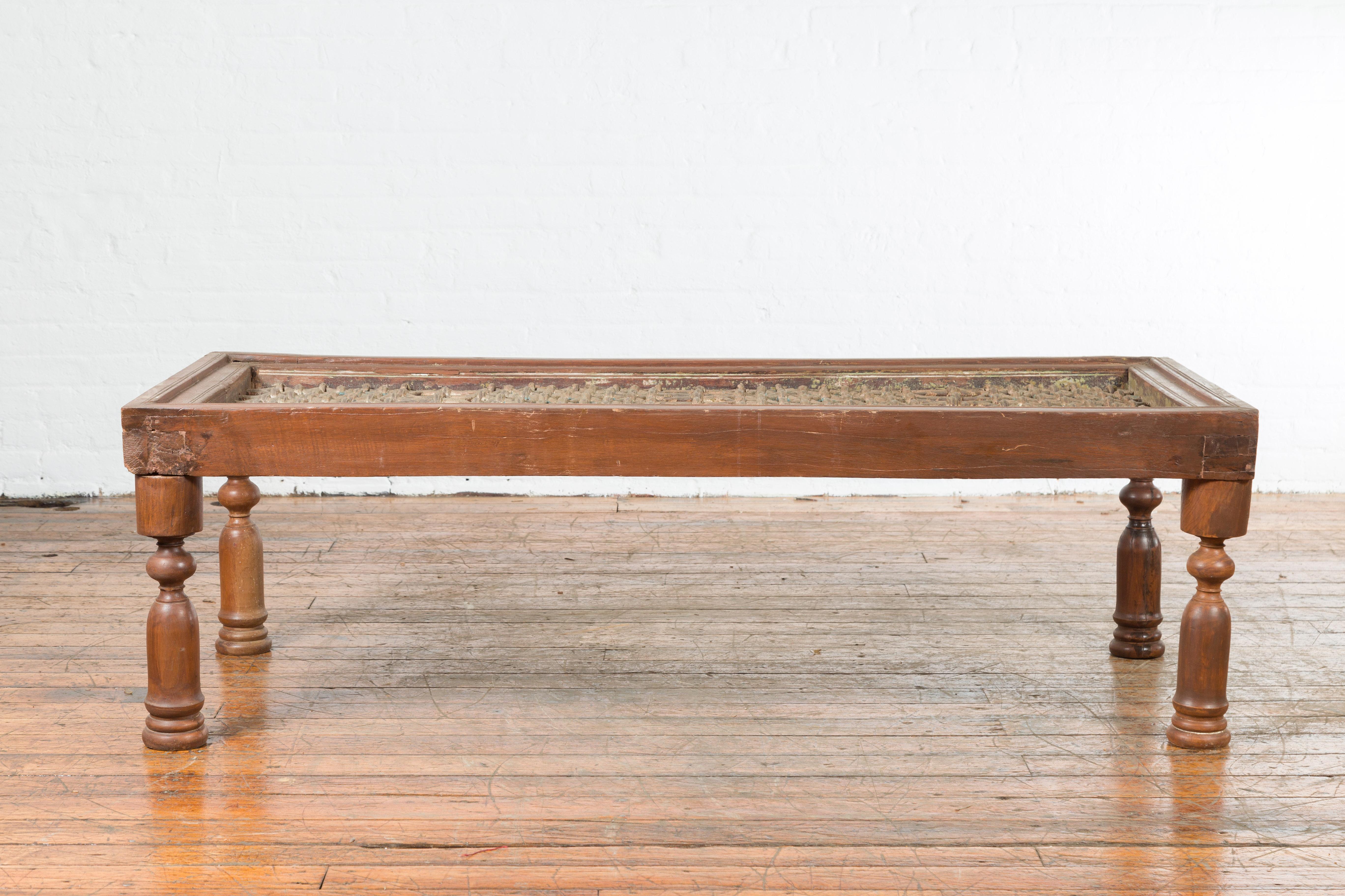 Une ancienne grille de fenêtre indienne du 19e siècle, transformée en table basse avec des pieds balustres. Créée en Inde au XIXe siècle, cette table basse présente un plateau en grille de fer à motifs géométriques, reposant sur quatre pieds