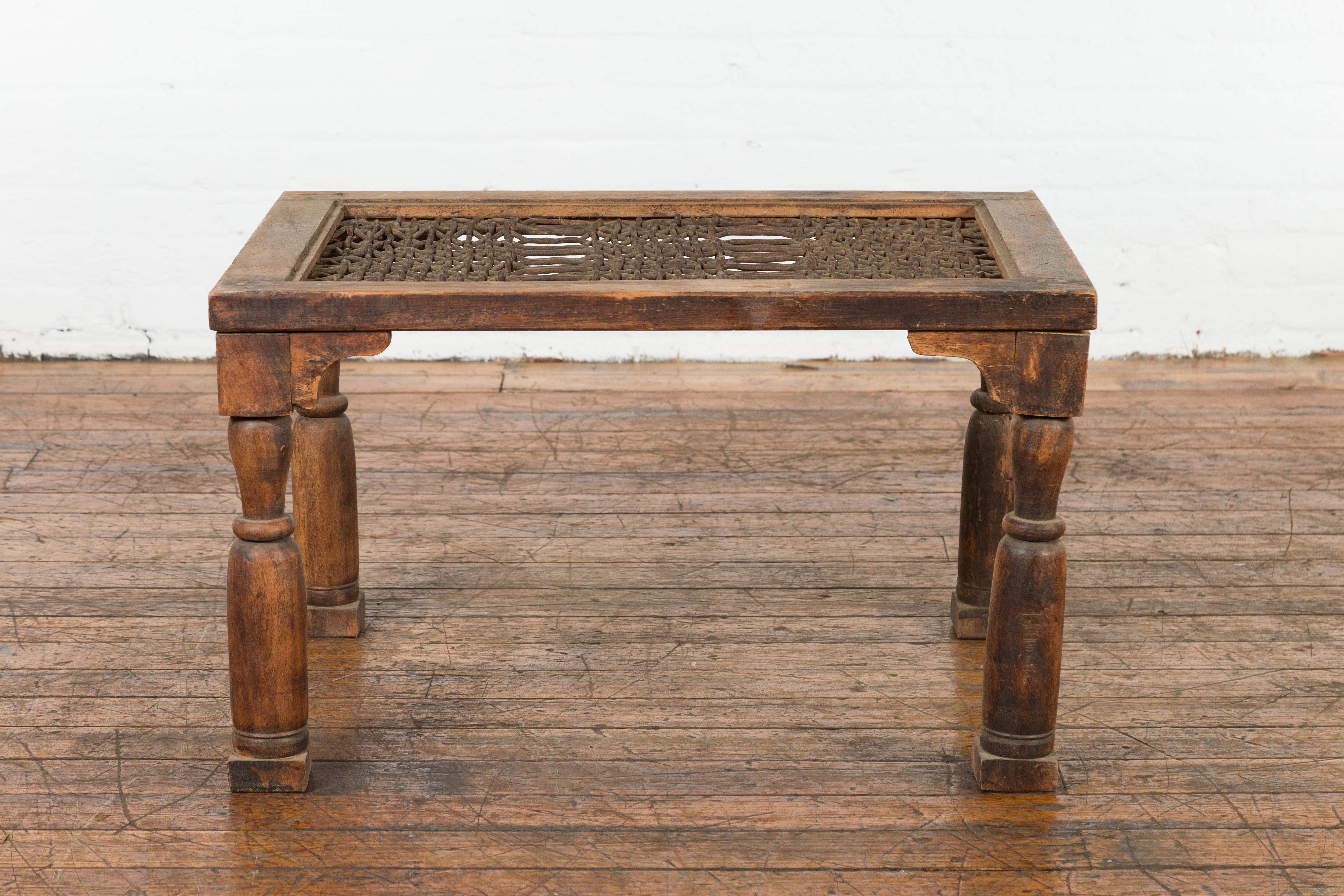 A rustic antique Indian window grate from the 19th century, made into a coffee table with carved spandrels, baluster legs and weathered appearance. Created in India during the 19th century, this coffee table charms us with its simple aspect and