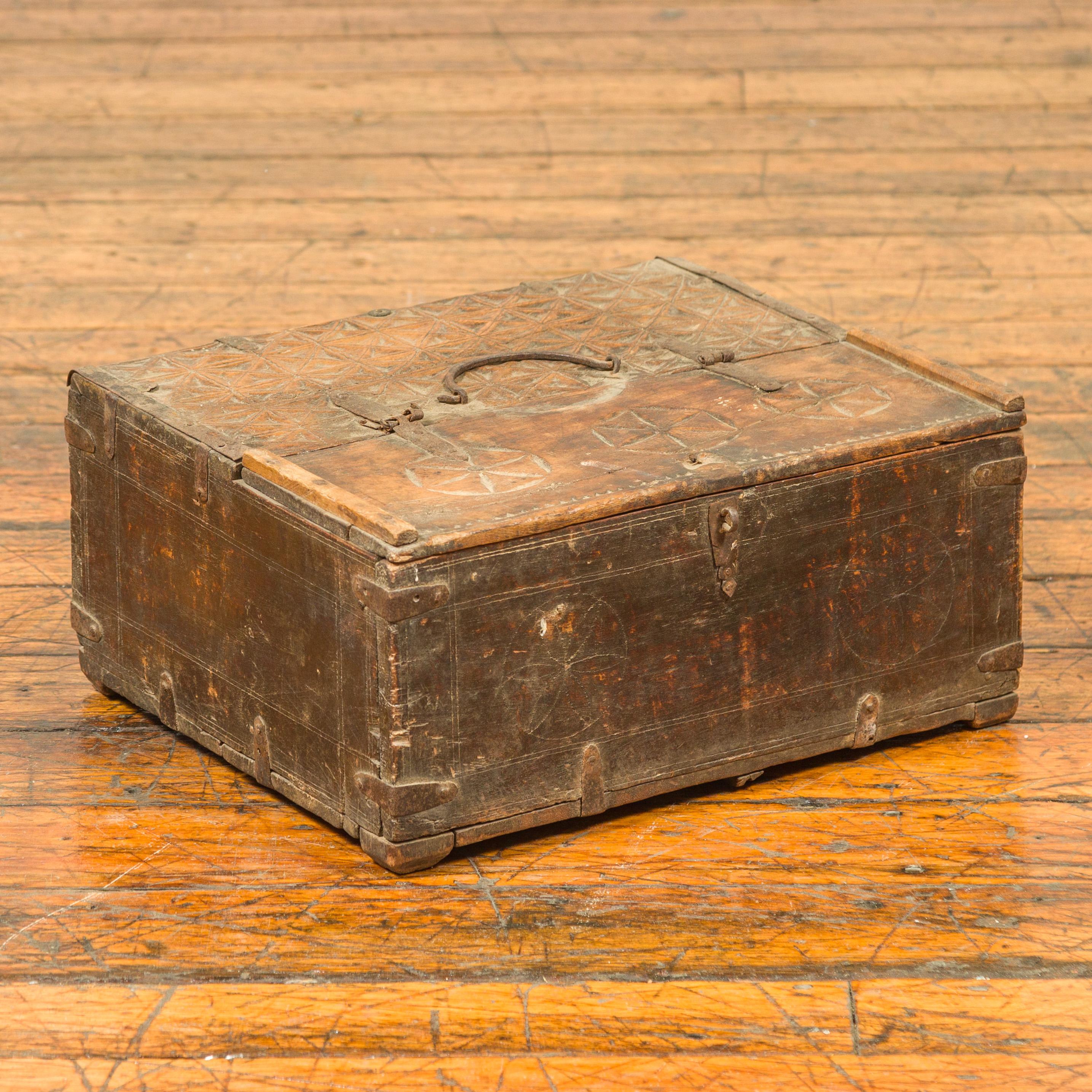 An antiue Indian wooden dowry box used by a merchant, with geometric design. Charming us with its weathered appearance and subtle geometric design, this dowry box showcases a rectangular top carved with geometric diamond and rosette motifs, and