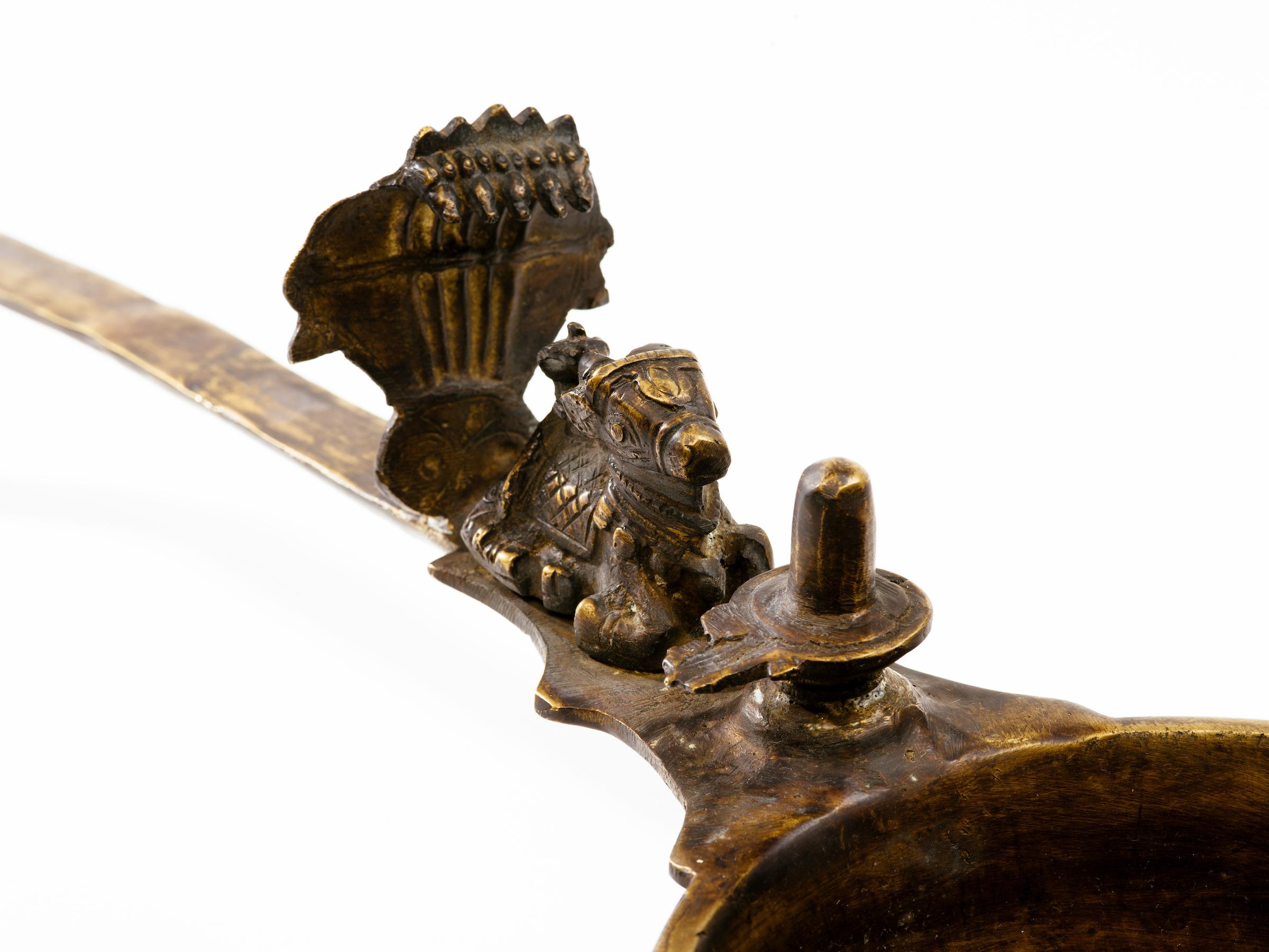 Finely hand-wrought bronze ceremonial oil lamp with figures of Lord Shiva's divine vehicle Nandi the bull, worshipping in front of a yoni lingam. Long handle with base, India, circa 20th century.