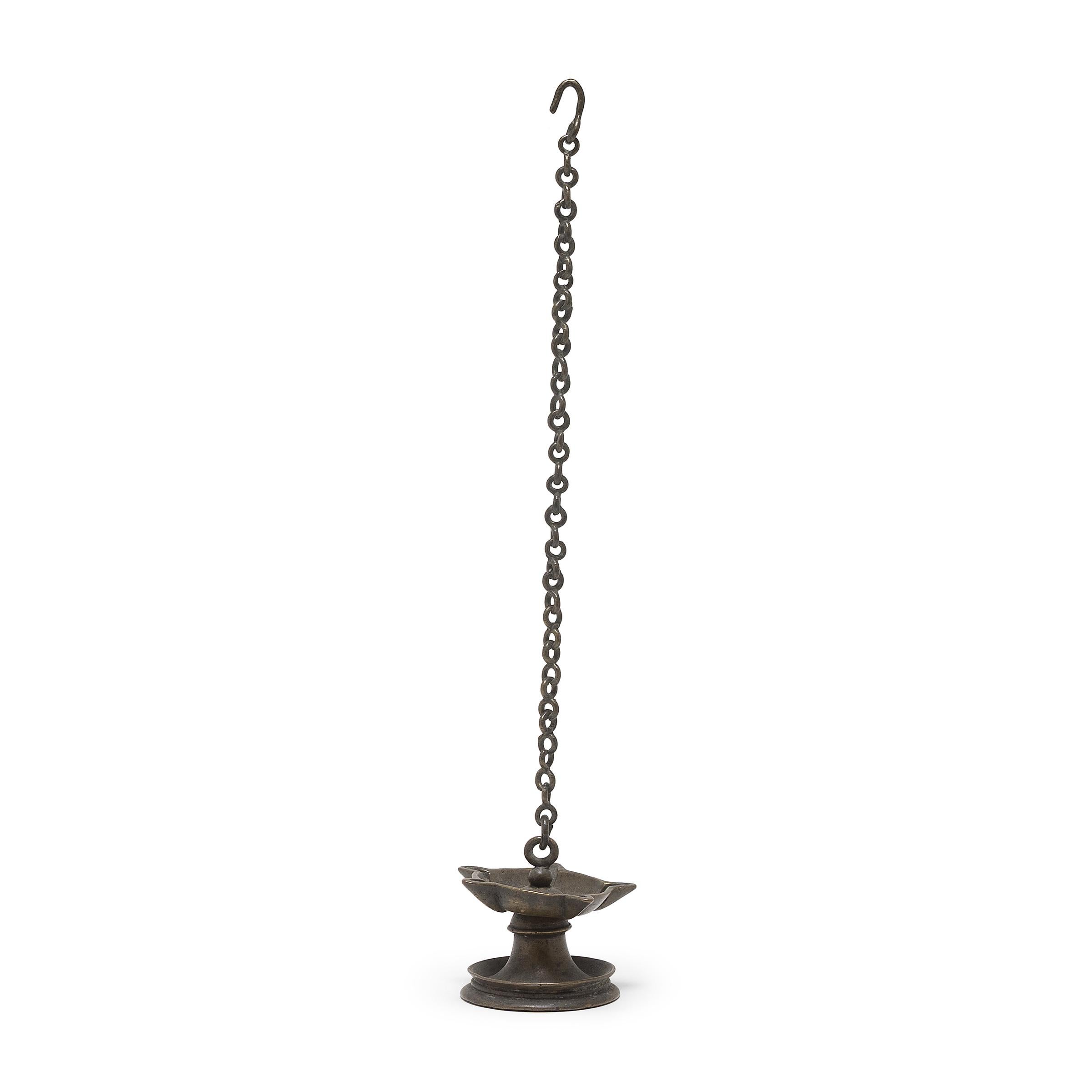 This small bronze object is a form of Indian hanging oil lamp known as a thookku vilakku, or pendant light. This example dates to the 19th century and features a shallow dish raised by a flared base and secured to a long chain and hook. The body of
