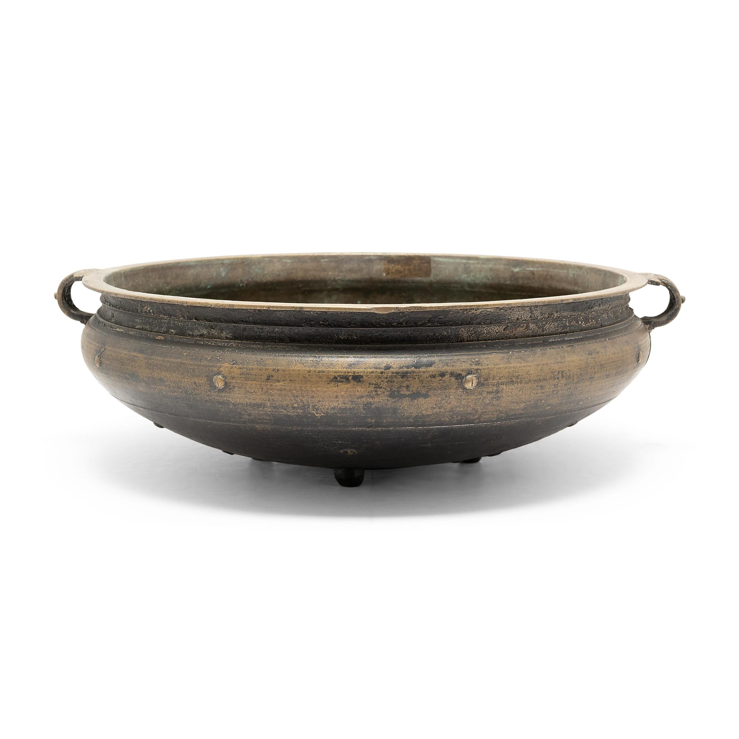 This shallow bronze bowl is an open fire cooking vessel from known as urli or uruli, used throughout southern India for preparing ayurvedic medicines and cooking large quantities of food for gatherings and ritual offerings. Cast of bell bronze using