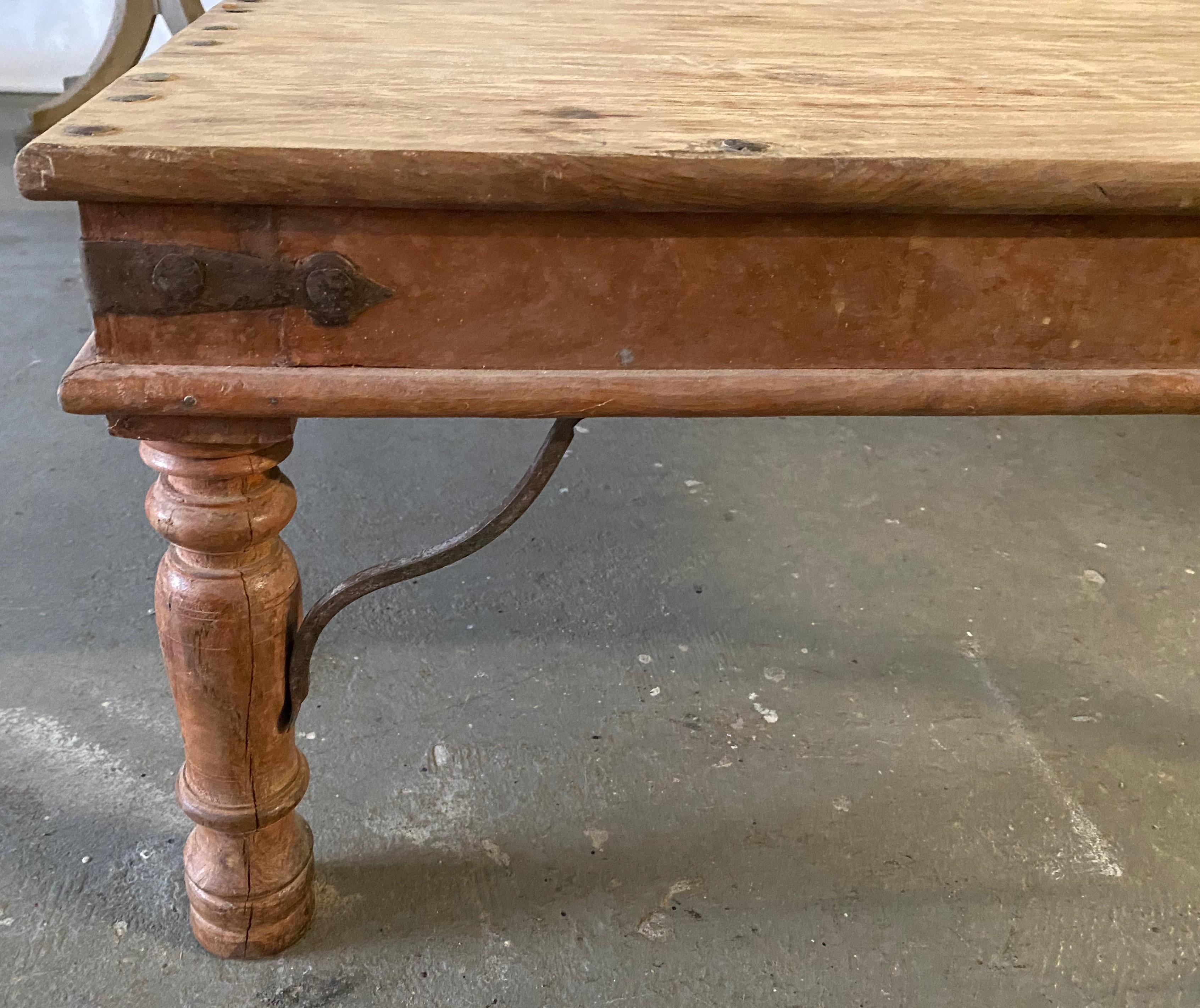 Vintage square coffee table created in India, accented with metal studs, resting on four turned baluster legs connected to the apron with iron stretchers. Nicely weathered appearance, this Indian coffee table will bring a touch of rustic