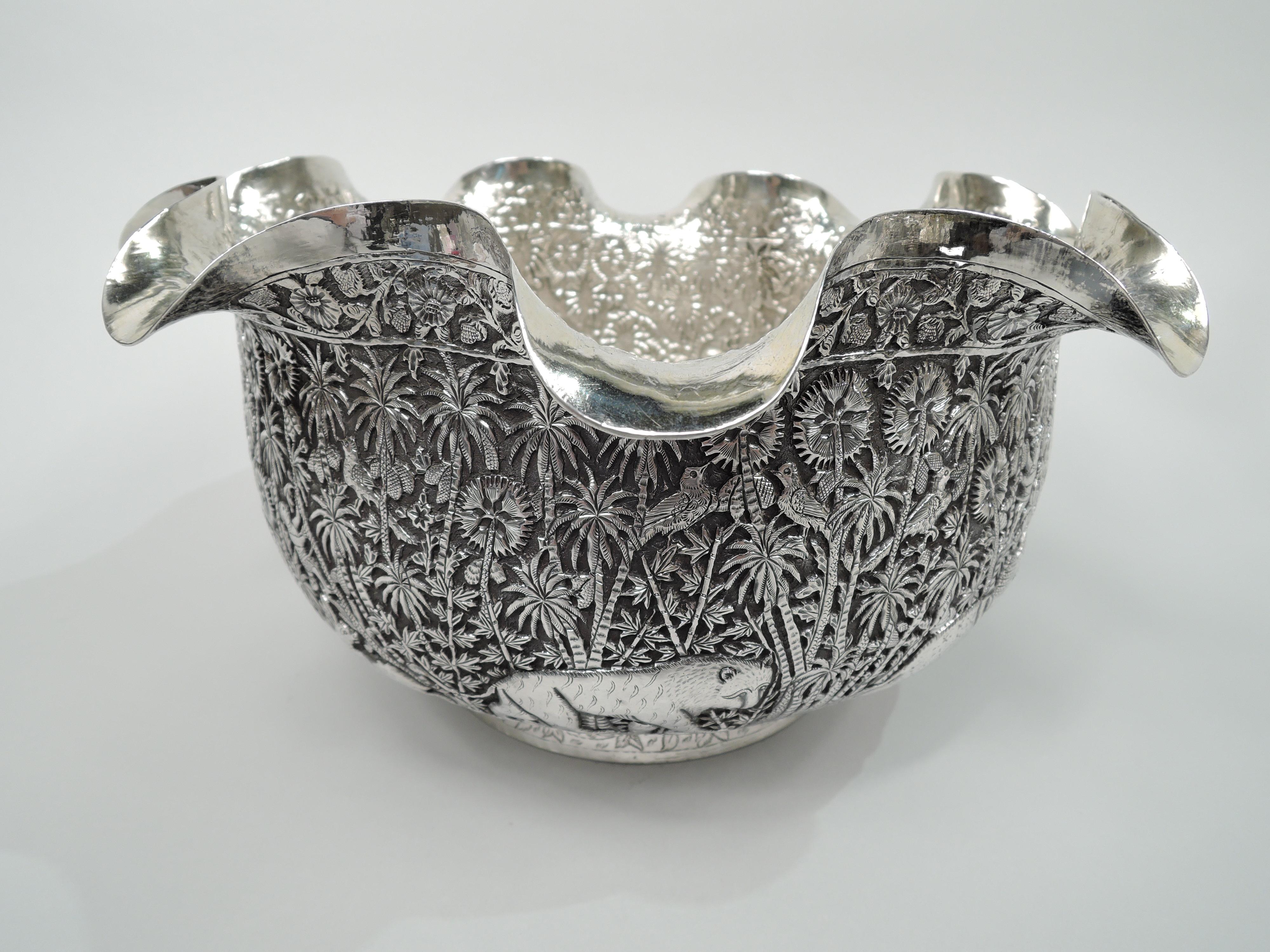 Indian Colonial silver bowl, circa 1890. Round with curved sides and wavy turned-down rim; short and canted foot. Dense repousse frieze depicting wild beasts loping through the jungle including a bear, antelope, jittery bunny, and caparisoned