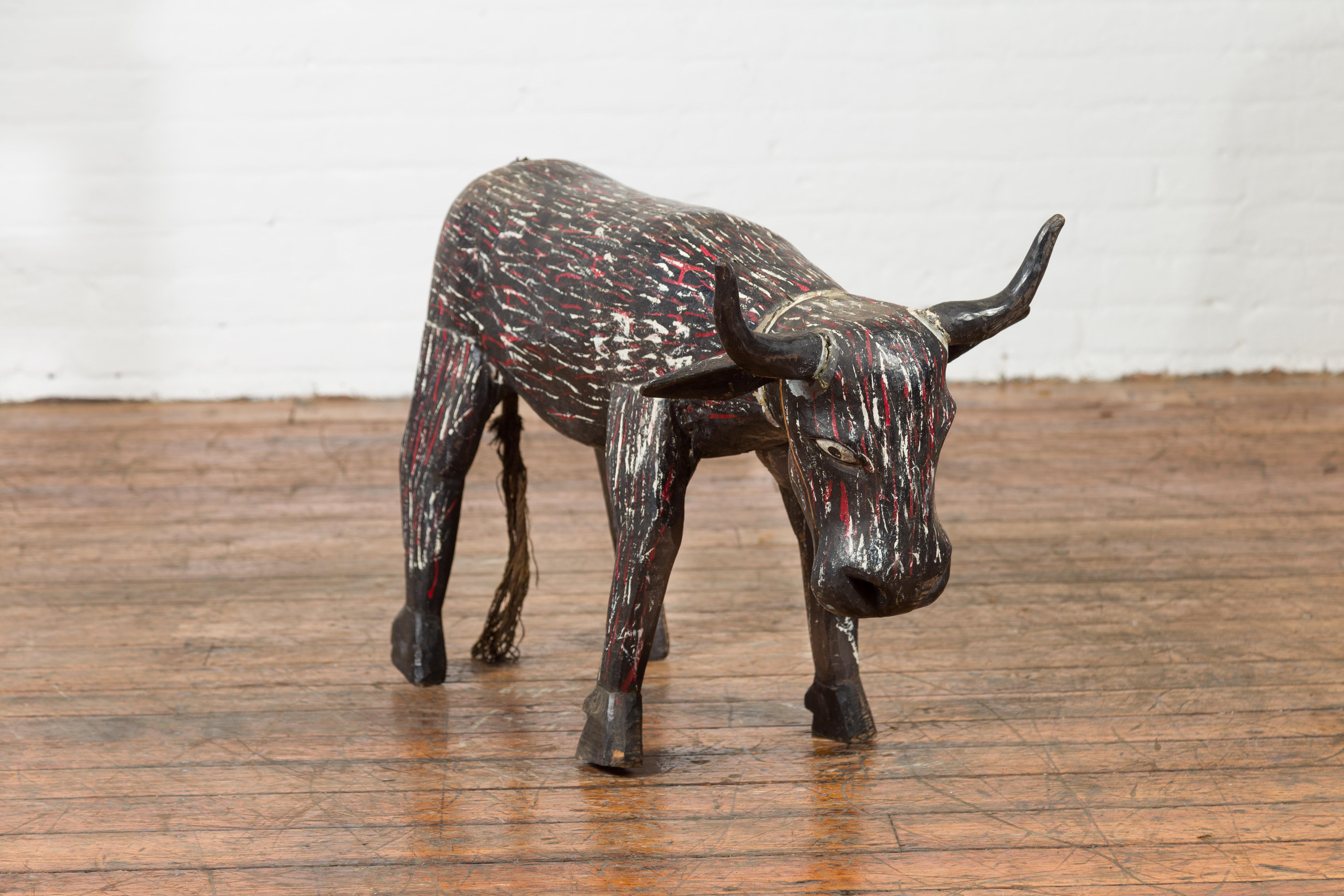 An Indian hand painted and carved wooden cow from the early 20th century, with nicely weathered patina. Created in India during the early years of the 20th century, this wooden cow sculpture charms us with its archaic features and aged appearance.