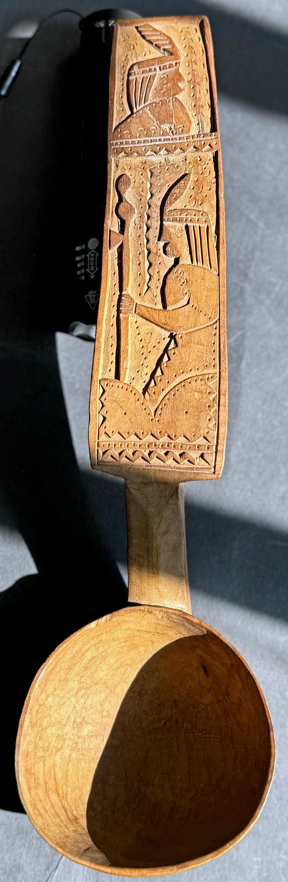 Hermoso y conmovedor, este cucharón de madera tallada a mano -una obra maestra del arte popular que muestra la influencia de los motivos modernos del Art Decó- representa dos figuras de indios americanos de perfil, cada una tallada en bajo relieve,