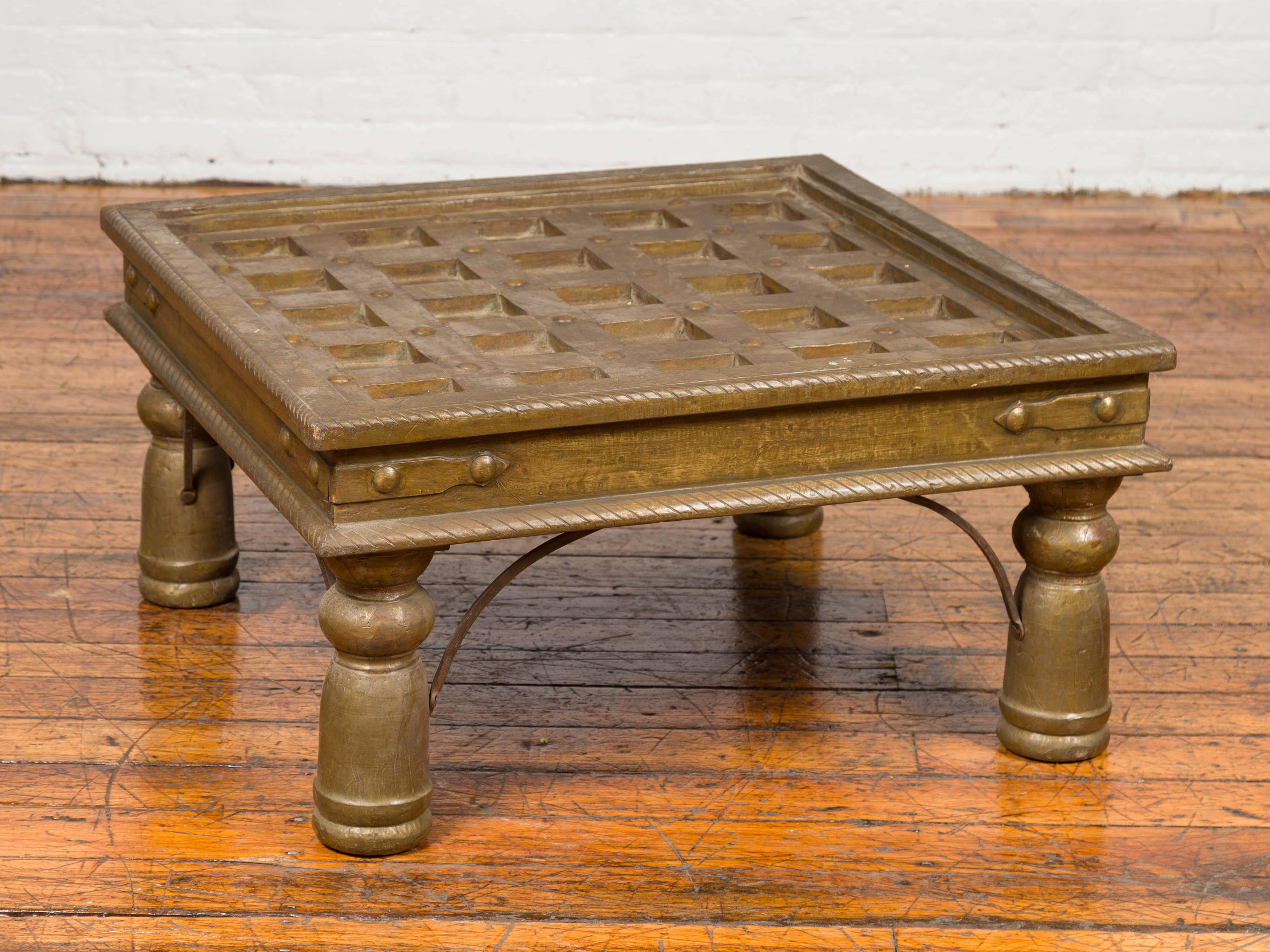 An antique Indian geometric wood and distressed brass window grate made into a coffee table. Born in India during the 19th century, this charming coffee table is made of a window grate, made of a wood composition structure bound with distressed