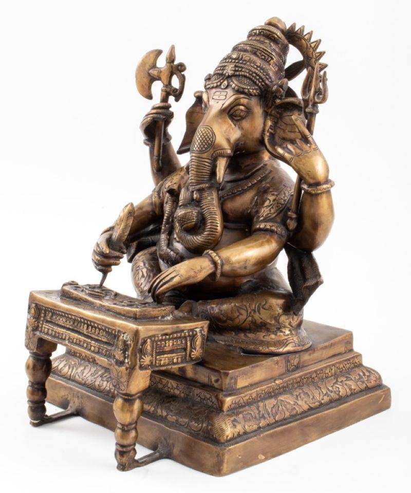 Indian gilt bronze statue sculpture of the Hindu Lord Ganesh cast with a cobra serpent encircling his belly, seated on a tiered base and writing the Mahabharata with two arms, the third and fourth arms wielding his Trishula / trident and an axe.