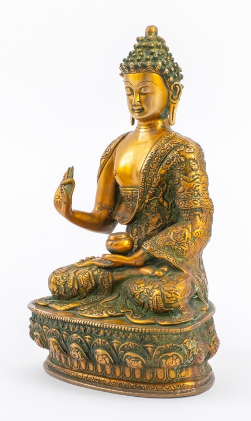 Indian gilt and verdigris brass statue sculpture depicting Buddha seated on a lotus pedestal with his right hand raised in the Vitarka mudra and left hand resting in his lap holding a vessel, his robes with scenes of Buddha's life in high relief,