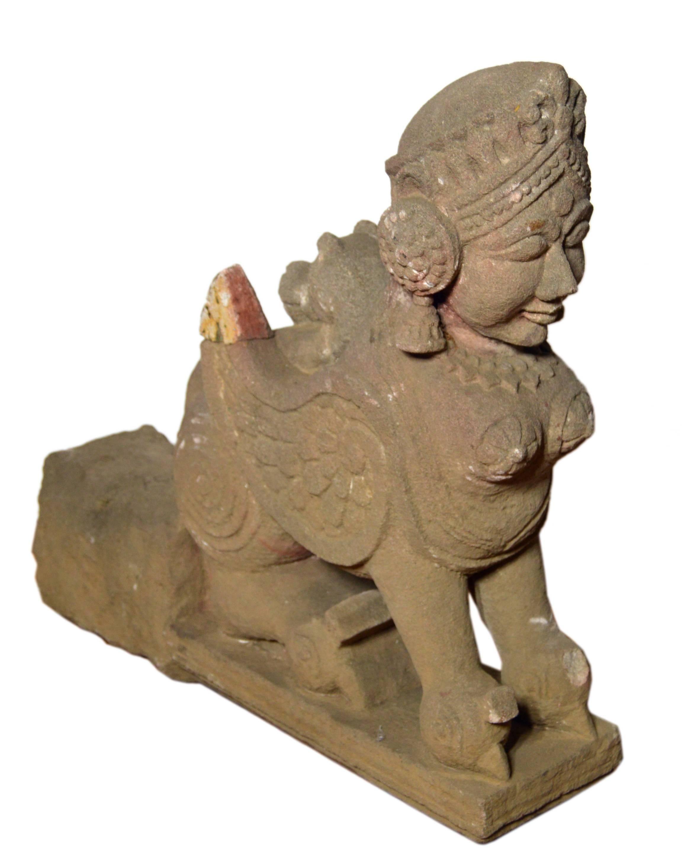 A 19th century Indian sphinx hand-carved stone sculpture, probably intended to adorn and protect a temple. The Indian stone sculpture features a sphinx figure, showcasing a winged lion body and a woman’s bust and head. This figure is decorated with