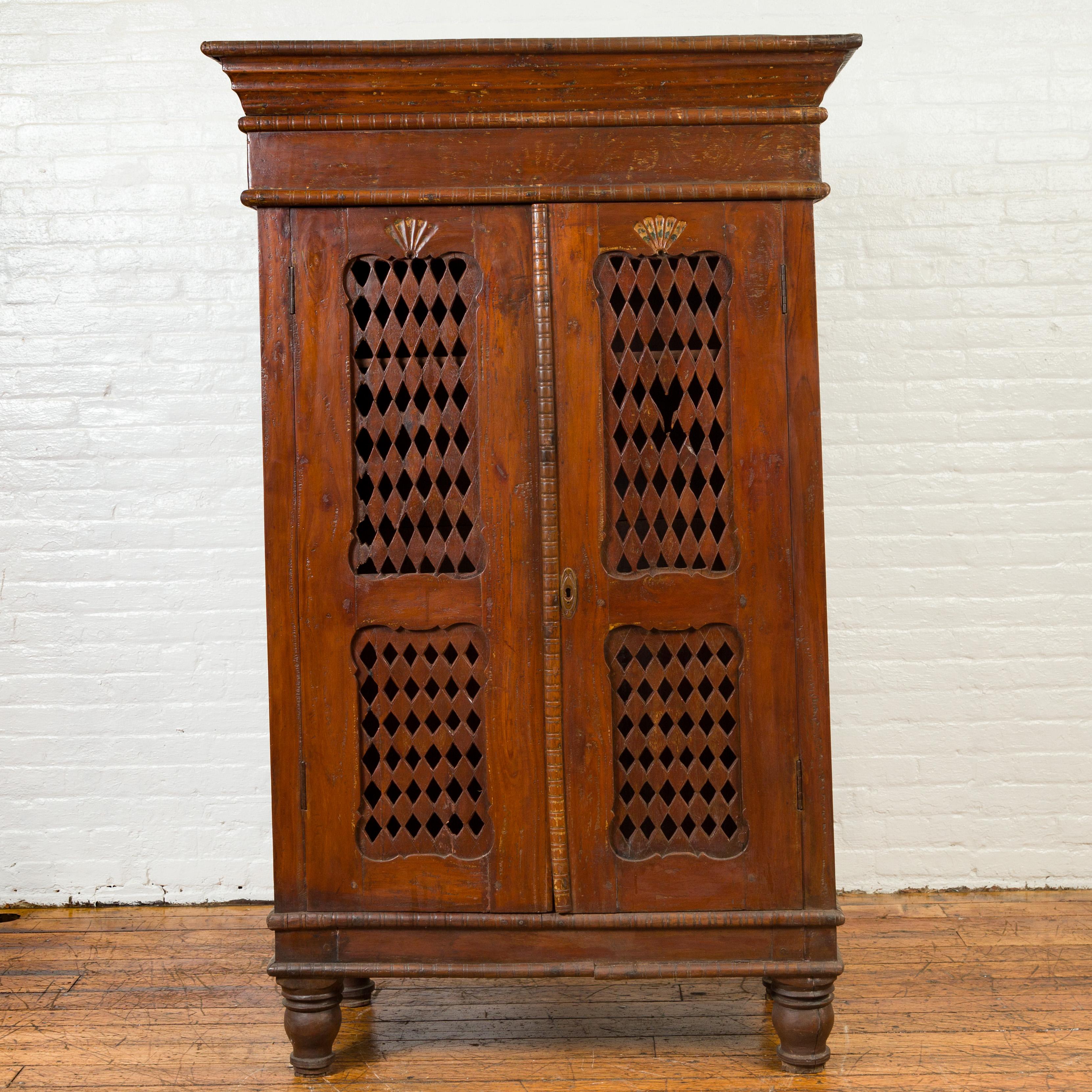 An antique Indian hand carved wooden kitchen cabinet from the 19th century, with open diamond design. Born in India during the 19th century, this cabinet features a beveled cornice sitting above two large doors. Each door is adorned with scrolling