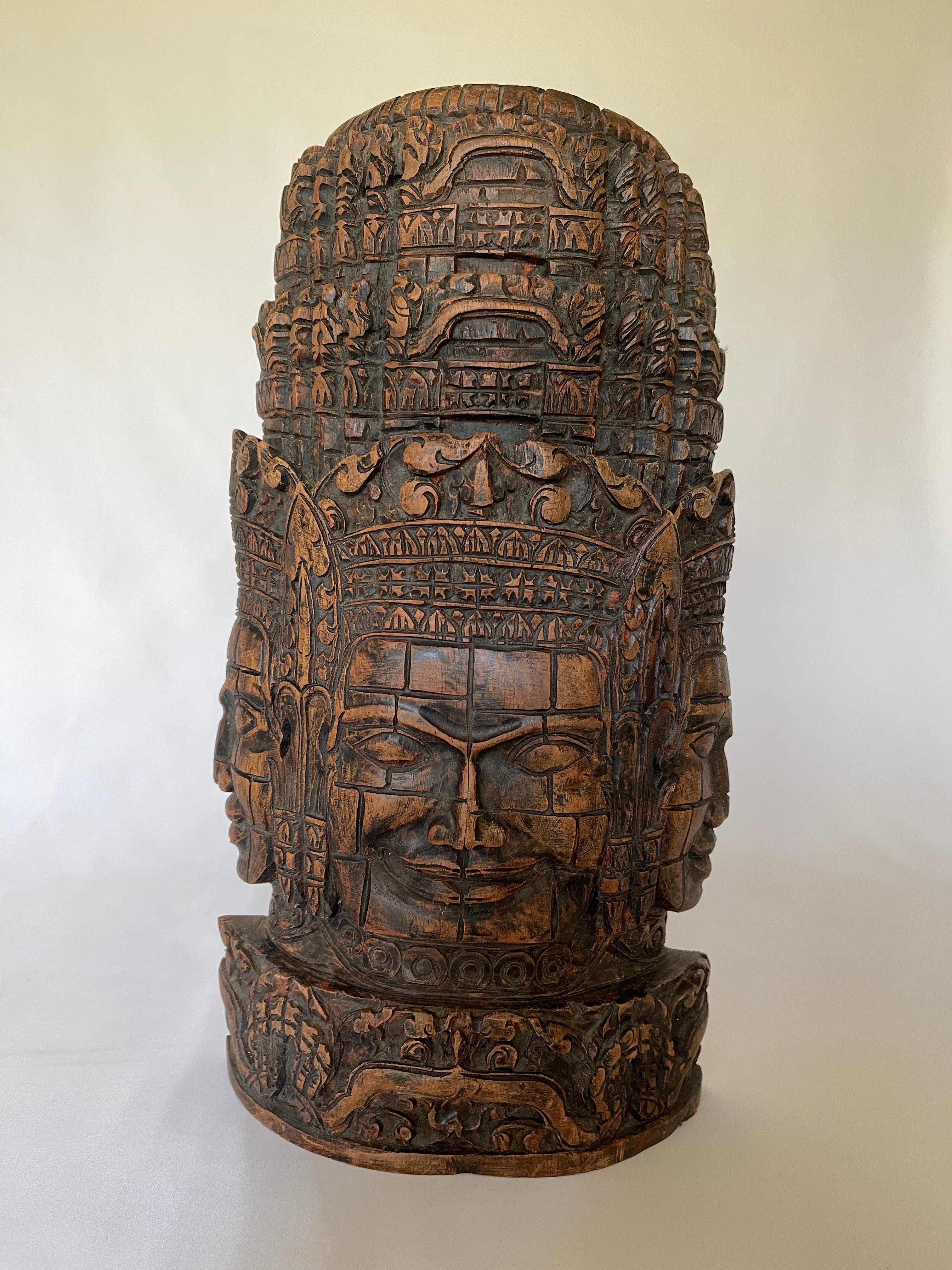 Vintage Indian hardwood Shiva Trimurti sculpture is intricately hand carved with three sides of the face of Lord Shiva, one of the 3 major Gods of the Hindu culture. He wears an elaborate headdress, and smiles benevolently.
 