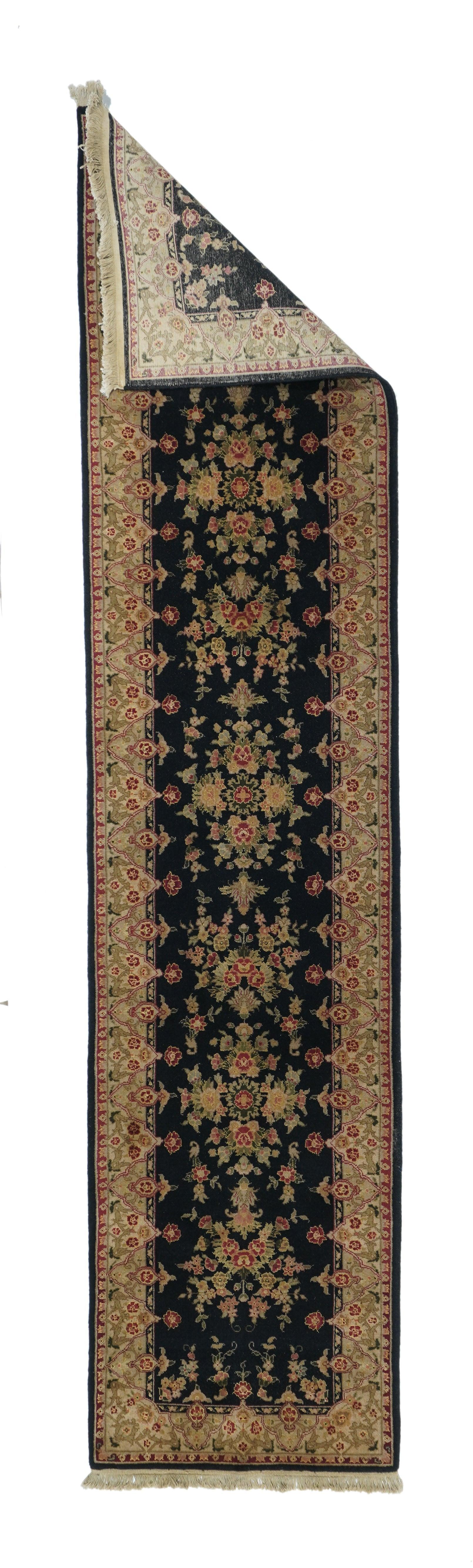 Runner indiano Kashan 2'3'' x 10'0''. Il campo nero a mezzanotte mostra sette elementi floreali aperti in forma di palmette fiammeggianti o semi-bouquet più naturali, con accenti in verde, rosso, corallo e sabbia. Bordo di triangoli invertiti.