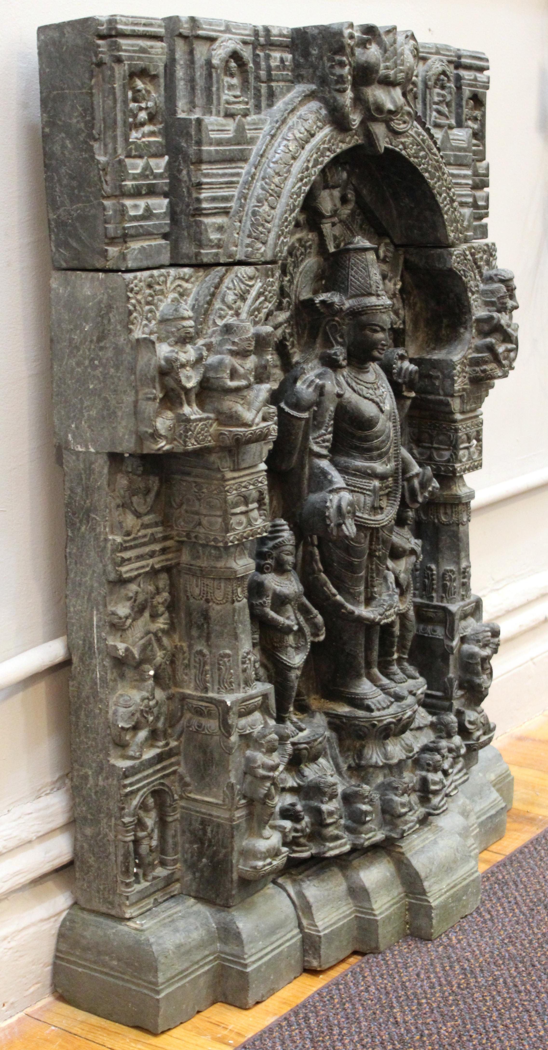 Indian Pala style stele of Bodhisattva Gautama Buddha carved into black basalt pieces, with a large carved central four-armed standing figure surrounded by smaller figures and carved elements surrounding the central stele, all atop a stepped
