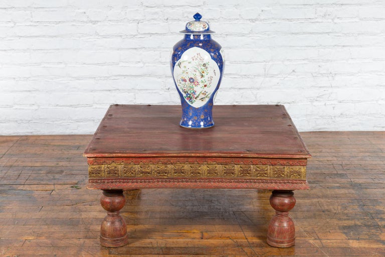 An antique Indian Primitive wooden coffee table from the 19th century with polychrome carved décor, turned baluster legs and studs. Created in India during the 19th century, this Primitive coffee table features a square planked top accented with a