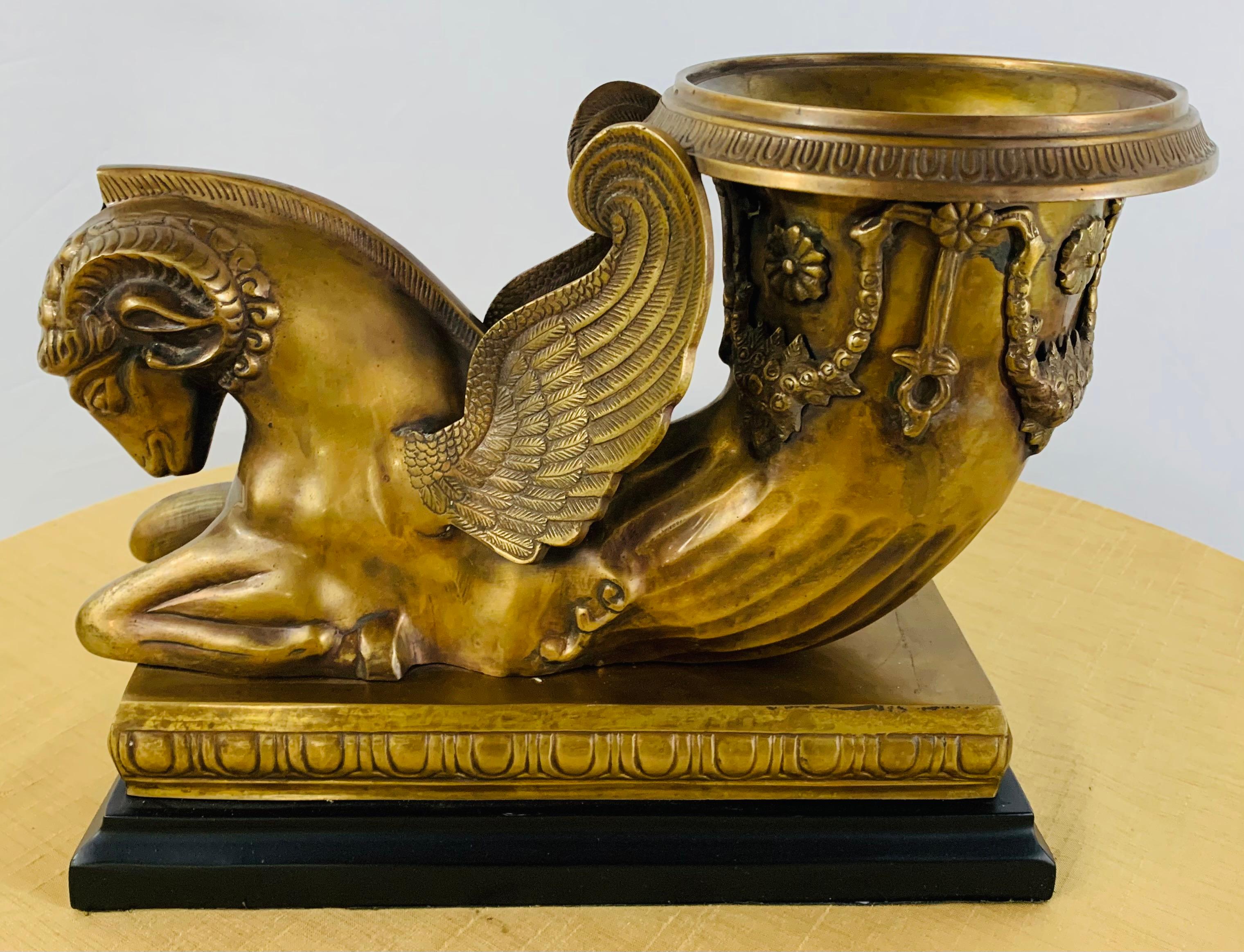 A stunning early 20th century sculpture of rython form terminating in a winged ram. The sculpture features intricate design of flowers on the rython and fine sculpting on the ram wings. The statue seats on a rectangular black metal base.
A one of