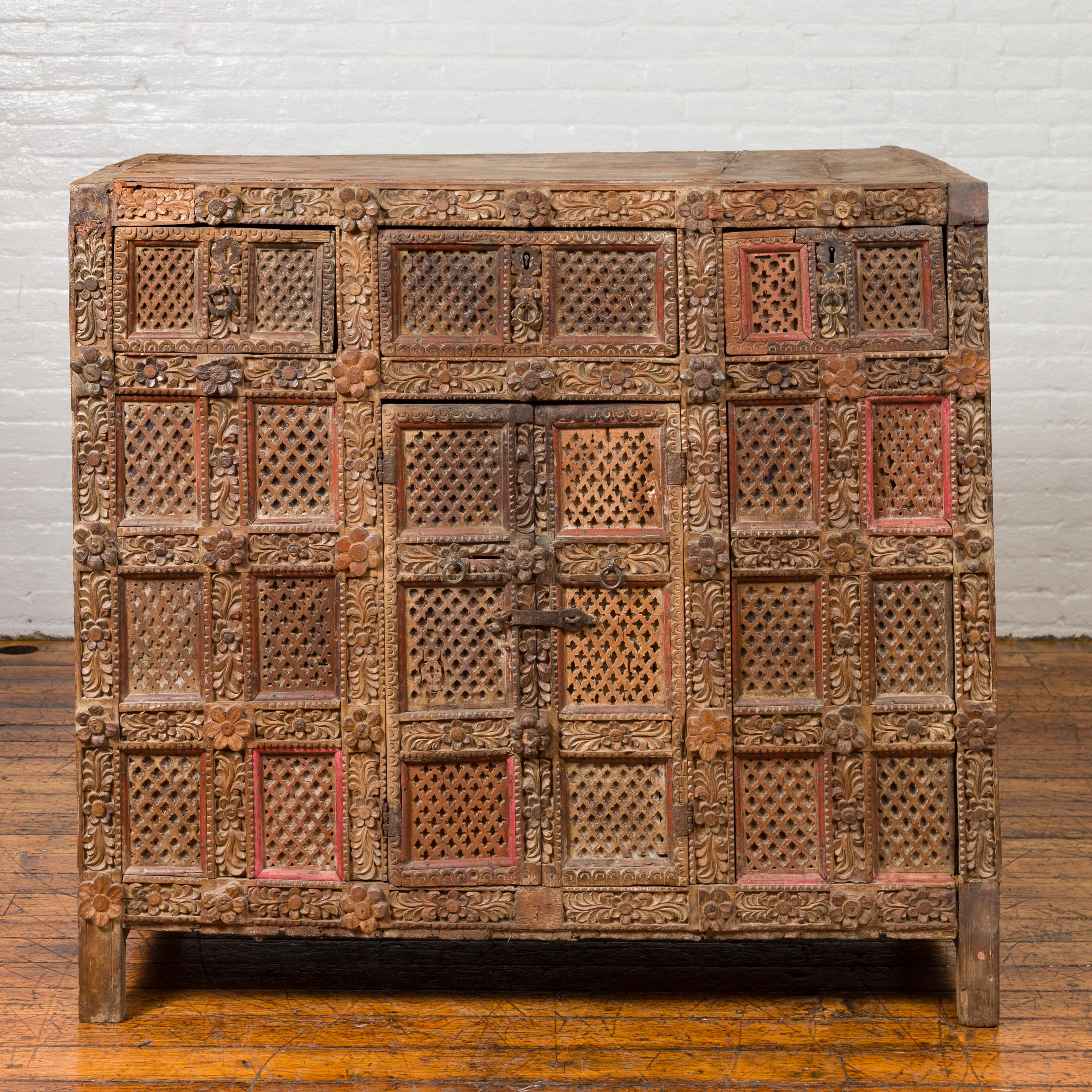 A large antique Indian rubbed wood palace cabinet from the 19th century, with floral-carved décor, pierced motifs and red patina. Born in India during the 19th century, this palace cabinet attracts our attention with its richly carved façade and