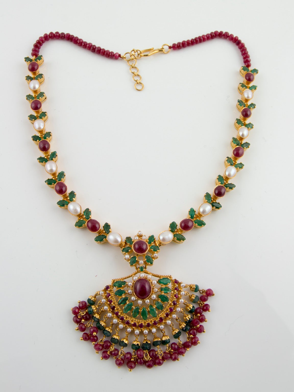 An elaborate traditional Indian Wedding set, comprising a necklet, bracelet & earrings of rubies, emeralds & pearls set in 22 carat gold. Necklet features a tasselled, fan-shaped pendant set with a deep red cabochon ruby flanked by semi-circular