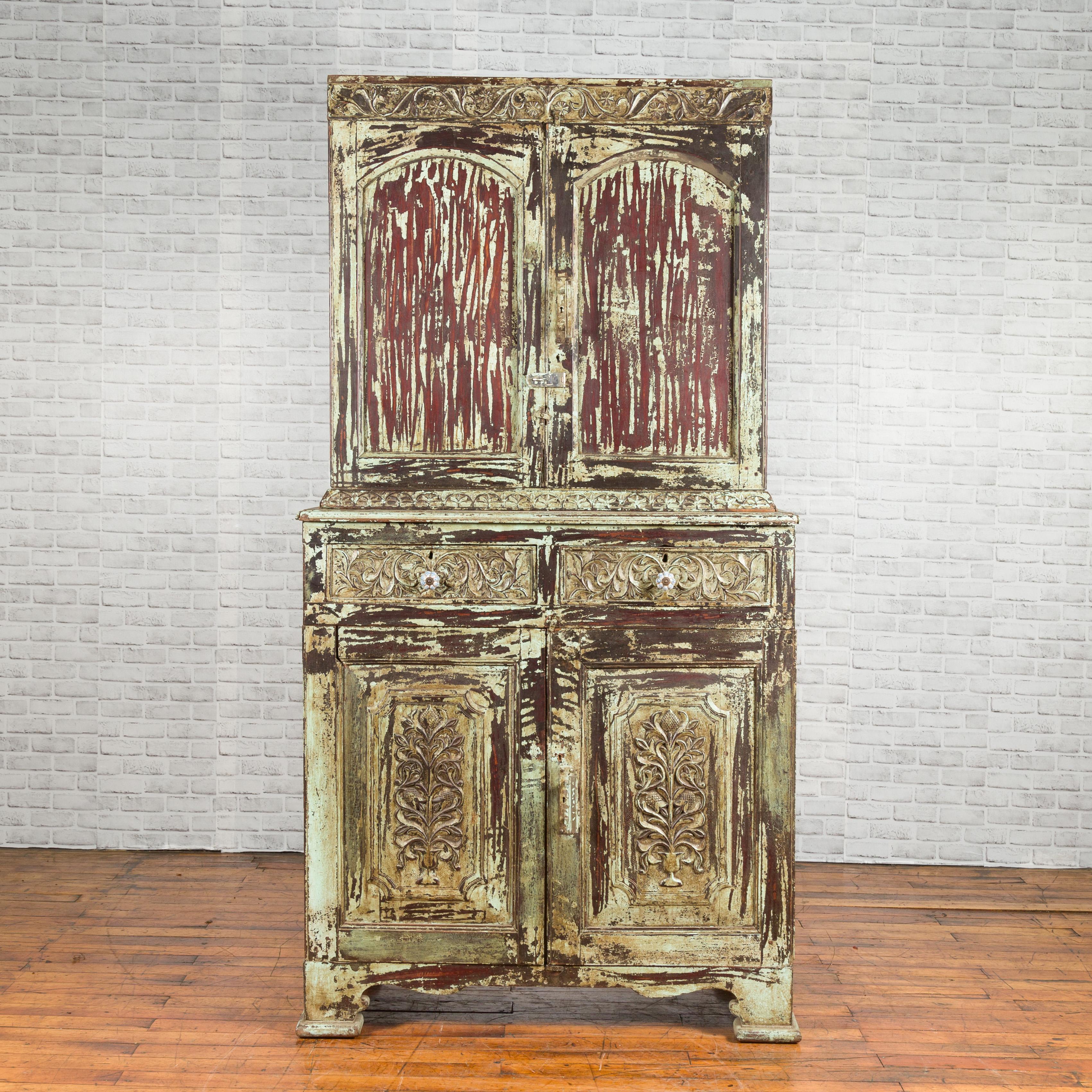 An Indian rustic painted wood cabinet from the early 21st century with carved scrolling foliage and distressed patina. Created in India during the early years of the 21st century, this tall buffet à deux-corps captures our attention with its carved