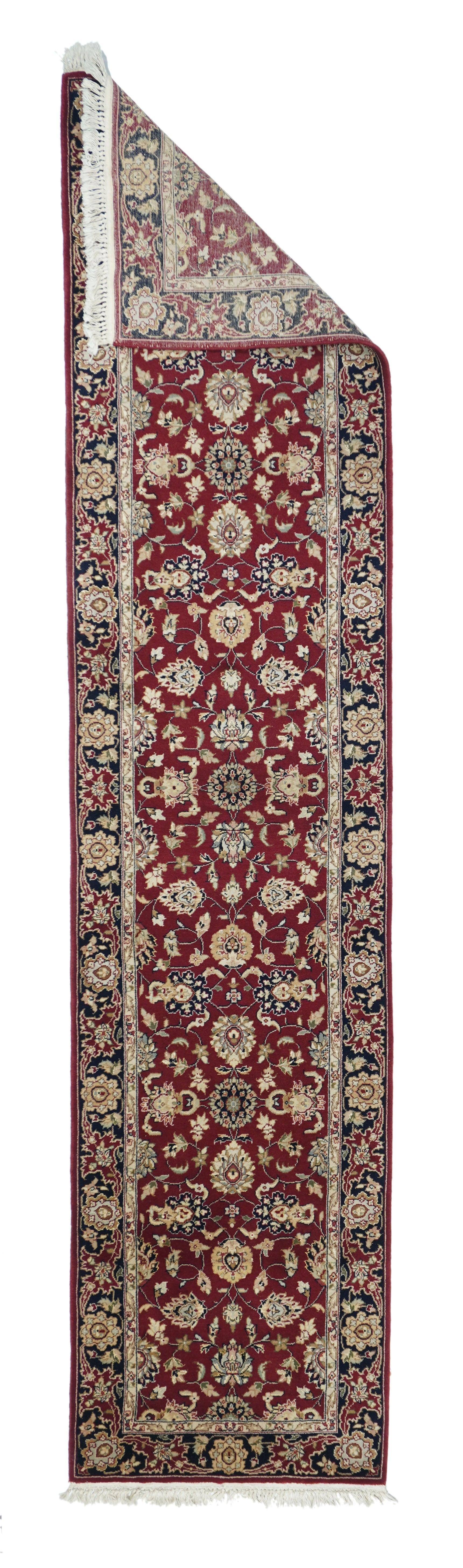 Runner indiano Tabriz 2'3'' x 10'0''. Il campo rosso chianti è centrato da tre rosette composte stratificate lungo l'asse verticale, con palmette a strati, arabeschi filiformi e boccioli di foglie dipendenti. Bordo principale nero navy con