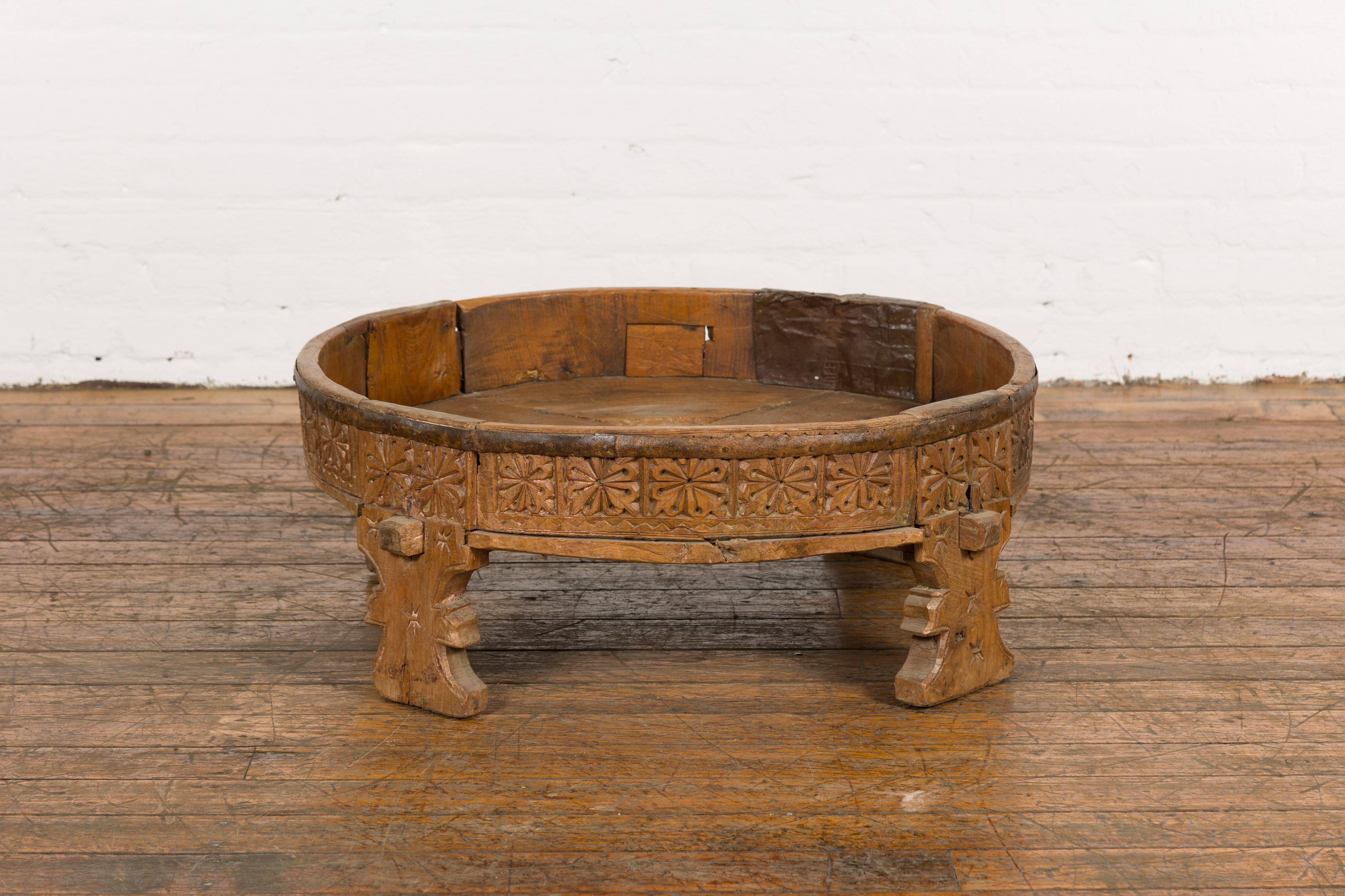 A Tribal Indian rustic teak wood Chakki grinder table from the 1920s with hand-carved geometric motifs, pierced center, carved feet and weathered patina. Step into the charm of traditional Indian craftsmanship with this 1920s tribal rustic teak wood