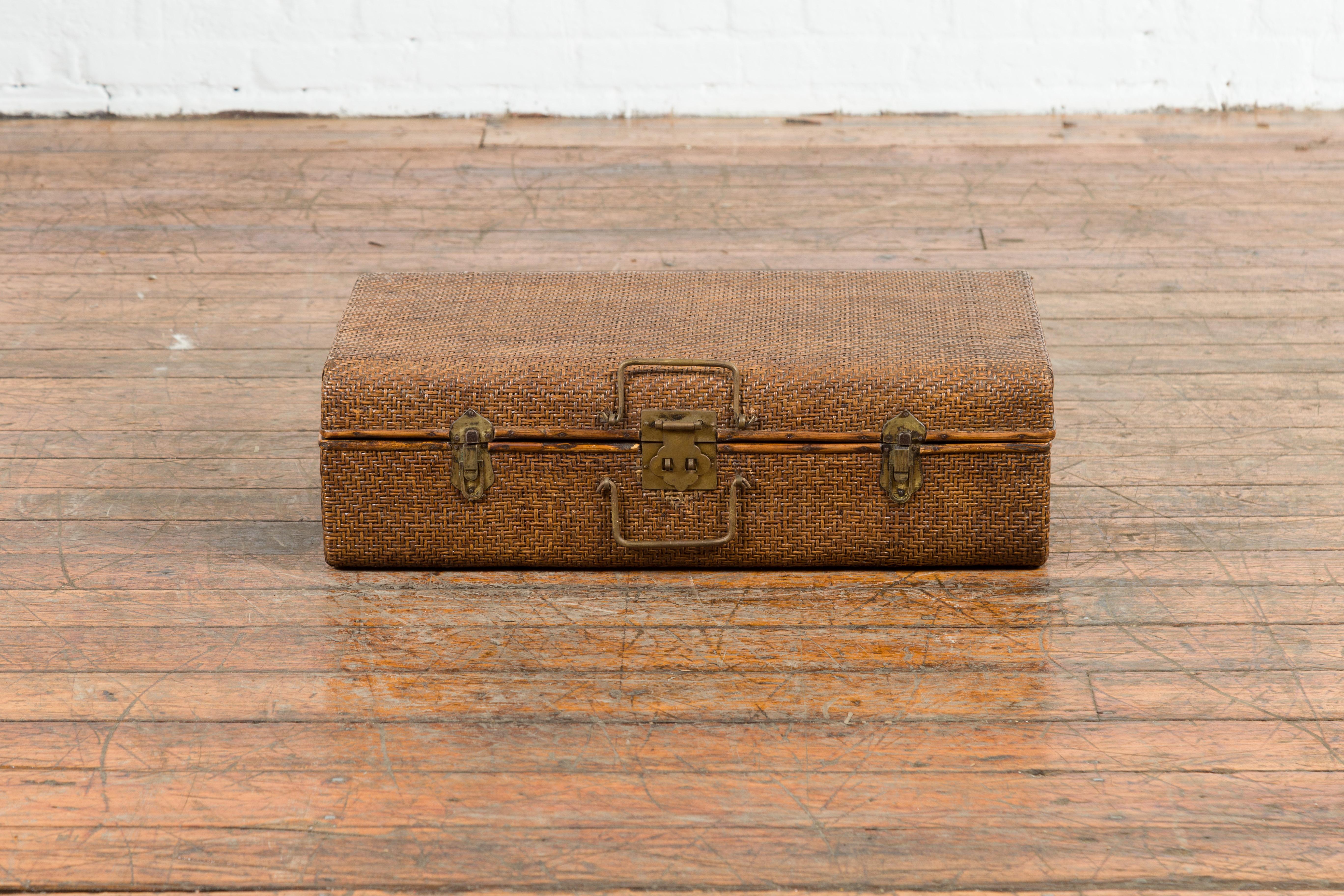 An Indian vintage bamboo and woven rattan suitcase from the mid 20th century, with brass hardware. Created in India during the midcentury period, this vintage suitcase features a rattan bound exterior surrounding a bamboo frame. Fitted with brass