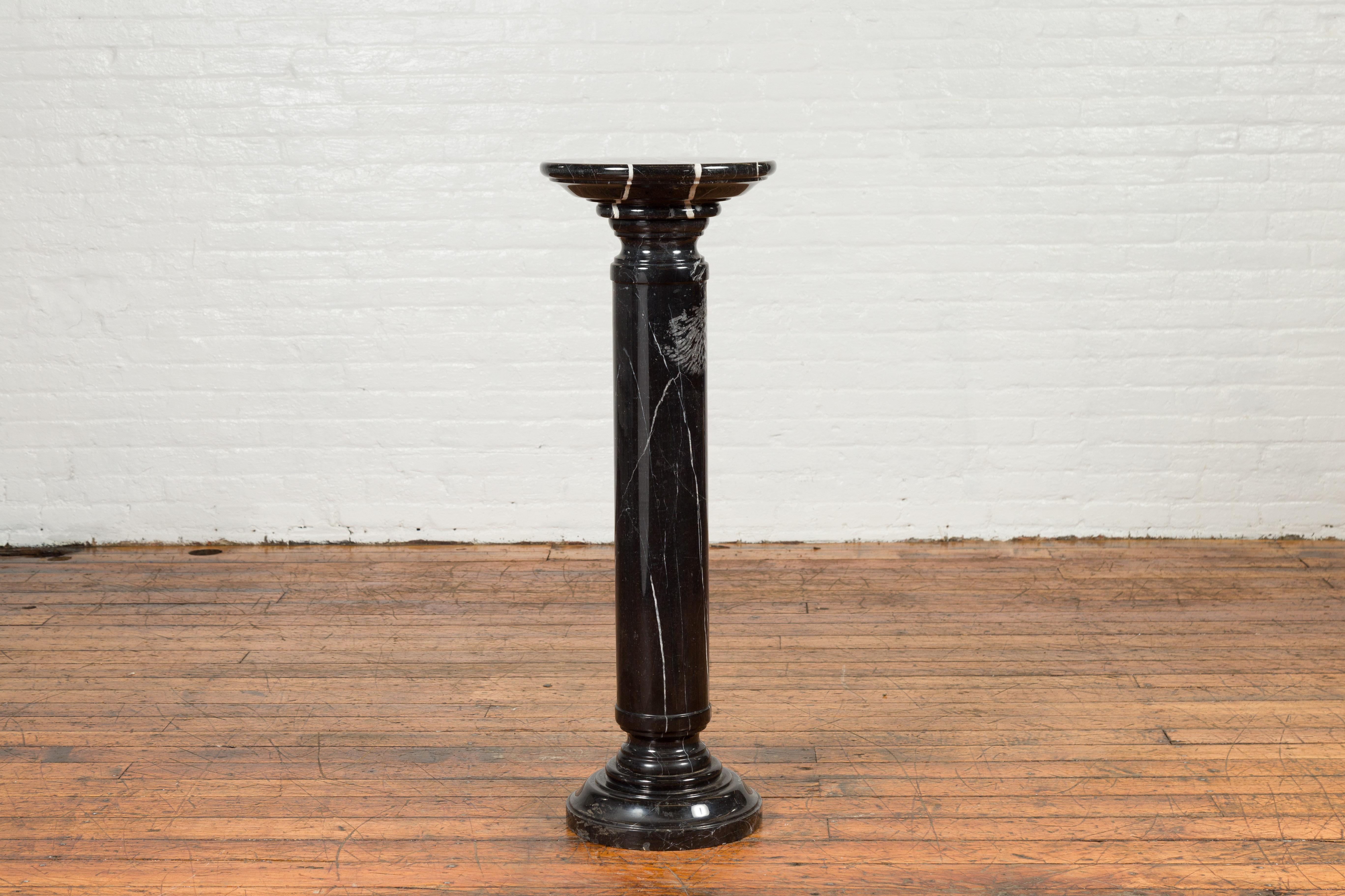 A Indian vintage black Carrara marble pedestal with circular top and cylindrical base. Crafted in India during the mid-20th century, this pedestal draws our attention with its black veined Carrara marble accented with white stripes and pure lines.
